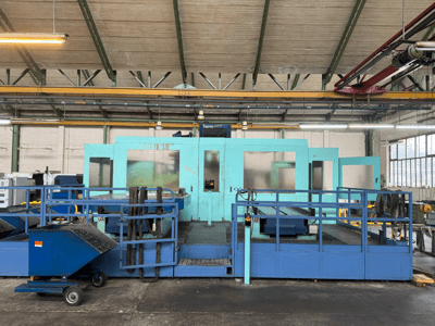 Máquina CNC industrial azul com painéis de proteção, vista frontal, com arrumação de ferramentas e um carrinho de recolha de resíduos na lateral.