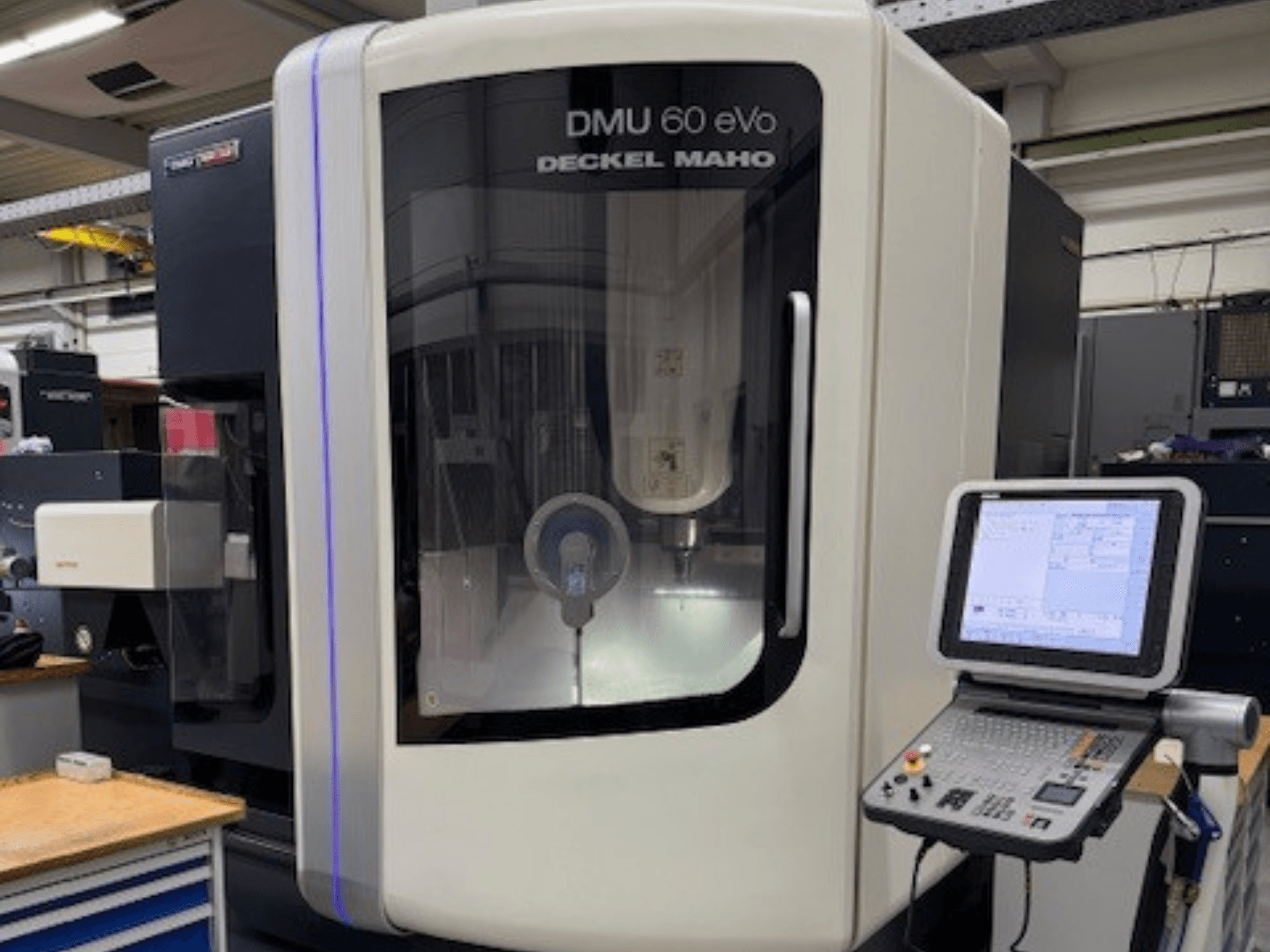 DMU 60 eVo da DECKEL MAHO, vista frontal de uma fresadora CNC com painel de controlo e ecrã, mostrando componentes de precisão.