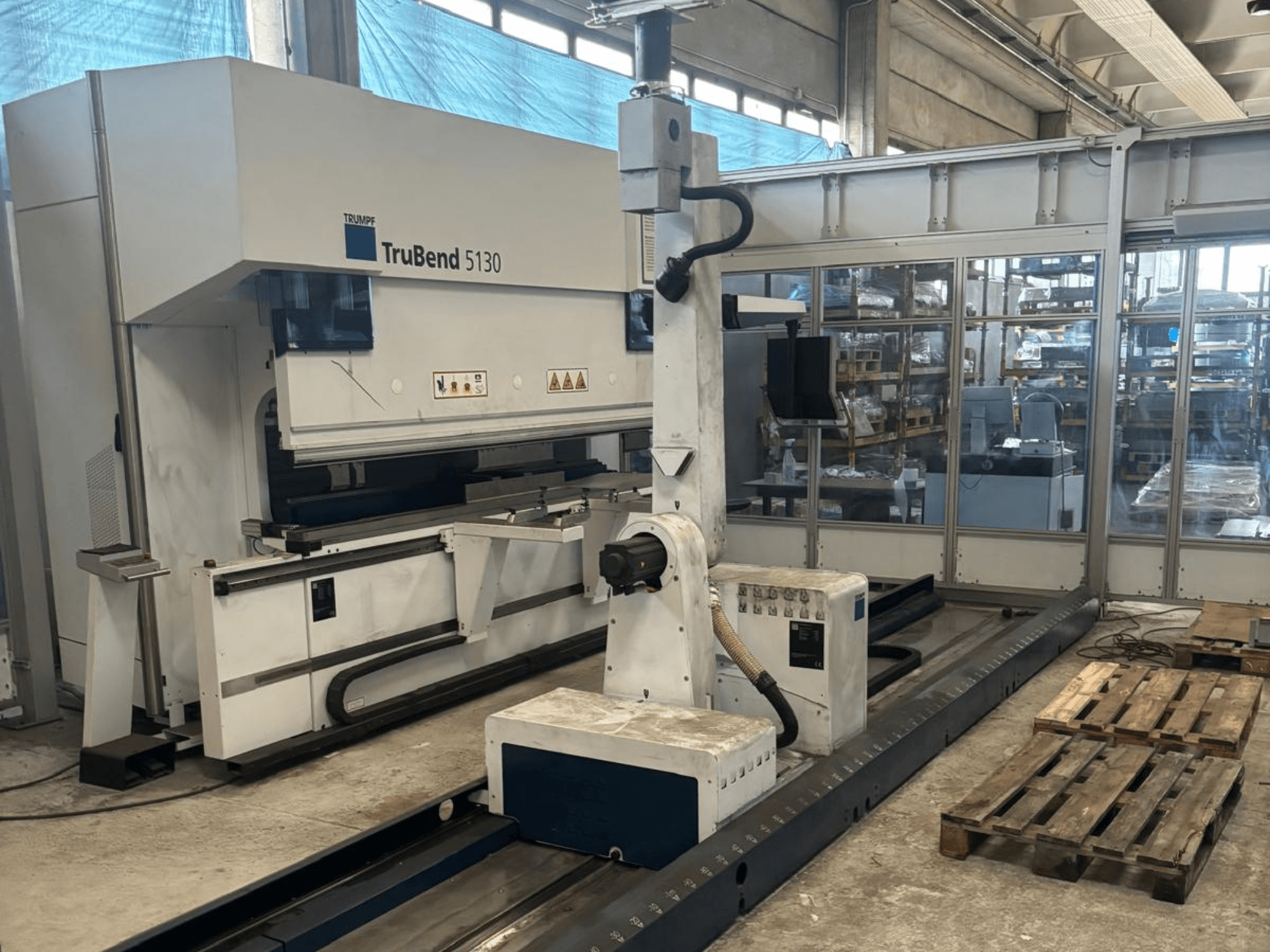 Máquina de dobragem TruBend 5130 da Trumpf, vista frontal, com painel de controlo e paletes numa fábrica.