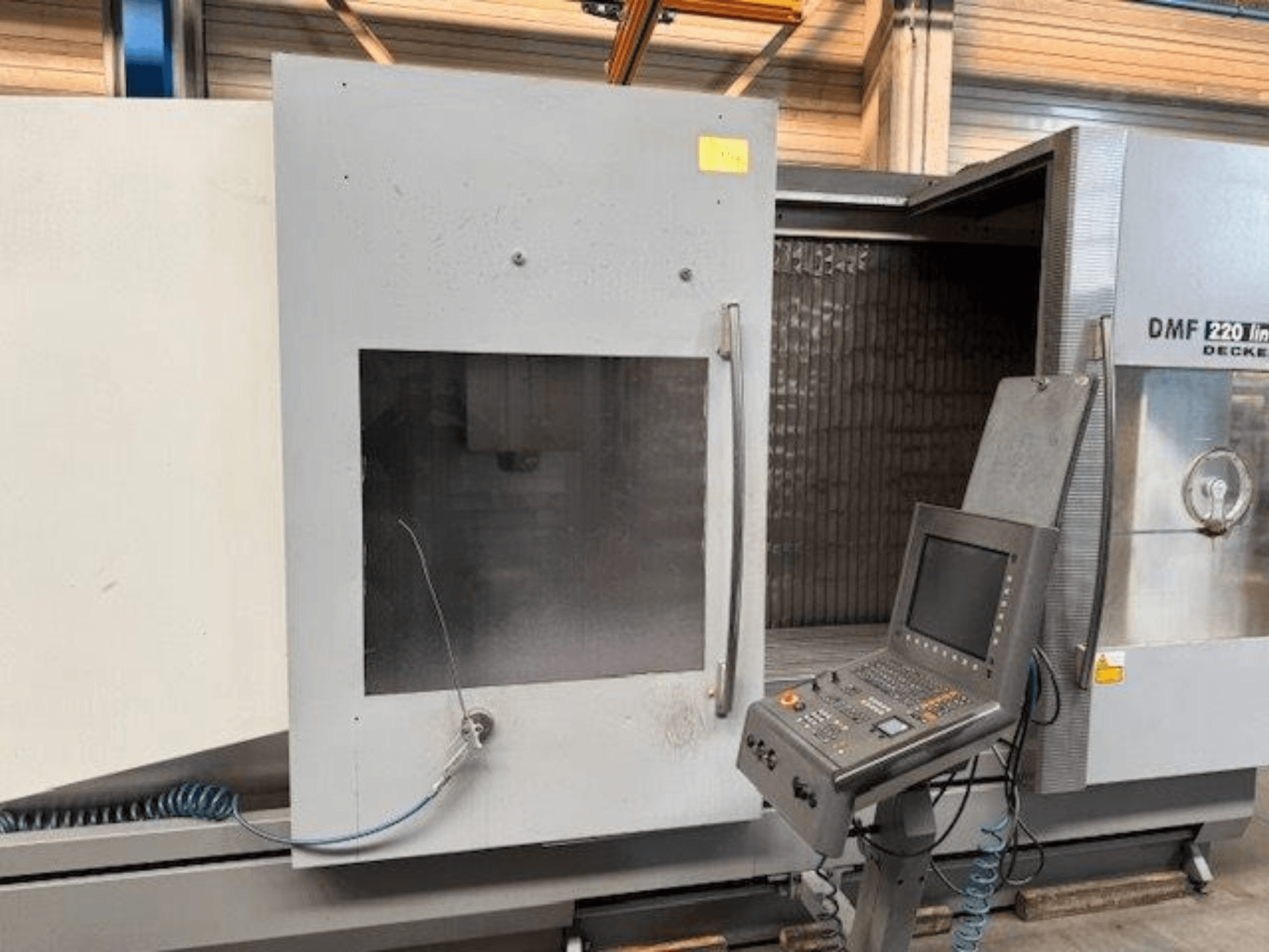 Vista frontal do centro de maquinação vertical DECKEL MAHO DMF 220 Linear, mostrando o painel de controlo e a porta da máquina aberta.