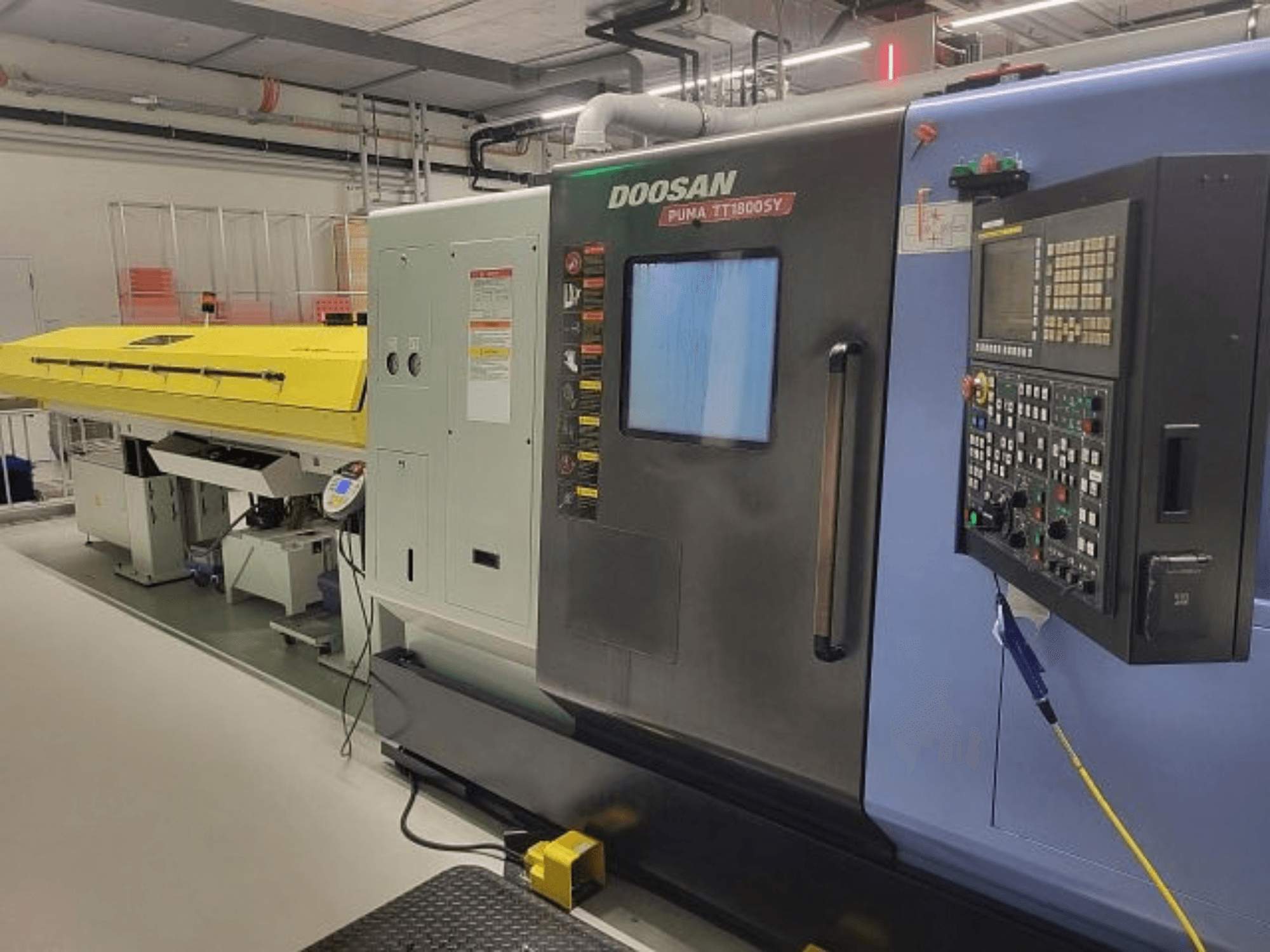 Centro de torneamento e fresagem DOOSAN PUMA TT 1800 SY, vista frontal com painel de controlo e cobertura amarela, ambiente industrial.