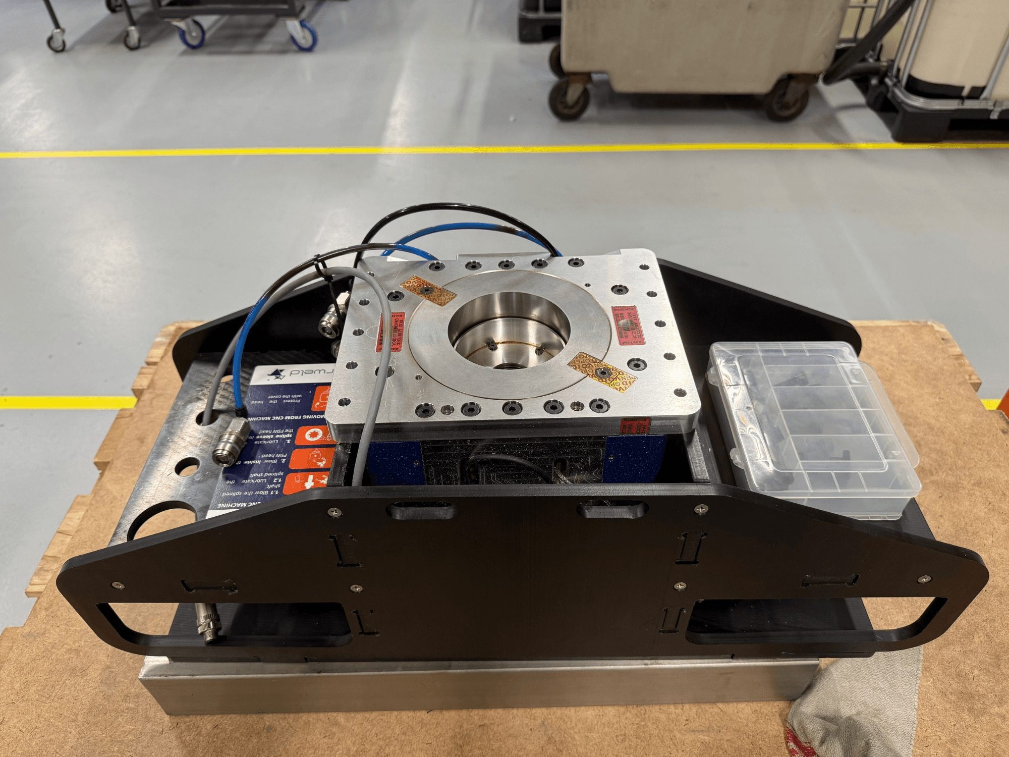 Componente metálico maquinado com cabos azuis, caixa de acessórios e base plana, mostrado de cima, ideal para aplicações mecânicas.