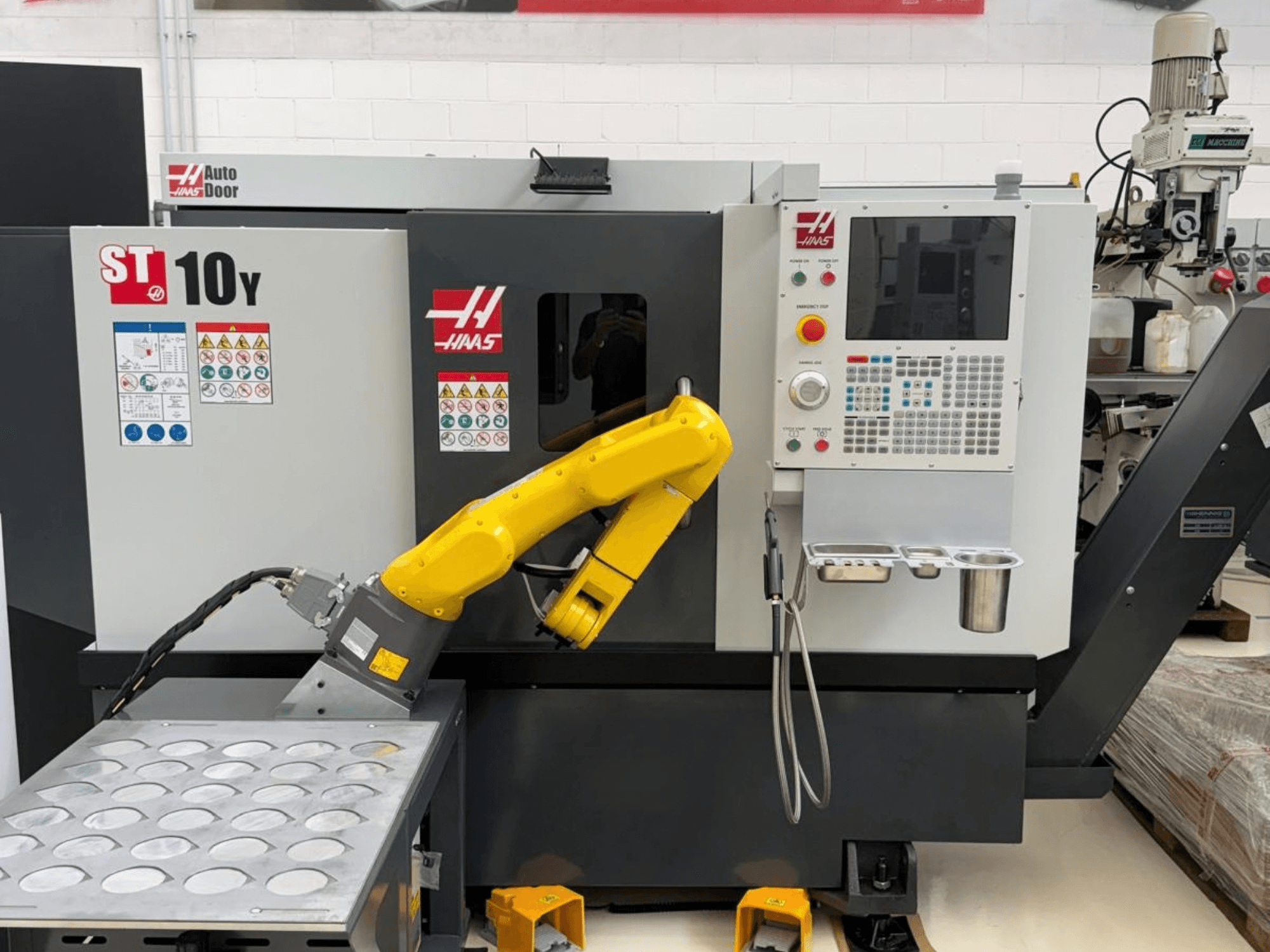 Torno horizontal Haas ST-10Y visto de frente, equipado com um braço robótico e um painel de controlo com tabuleiros para porta-ferramentas.