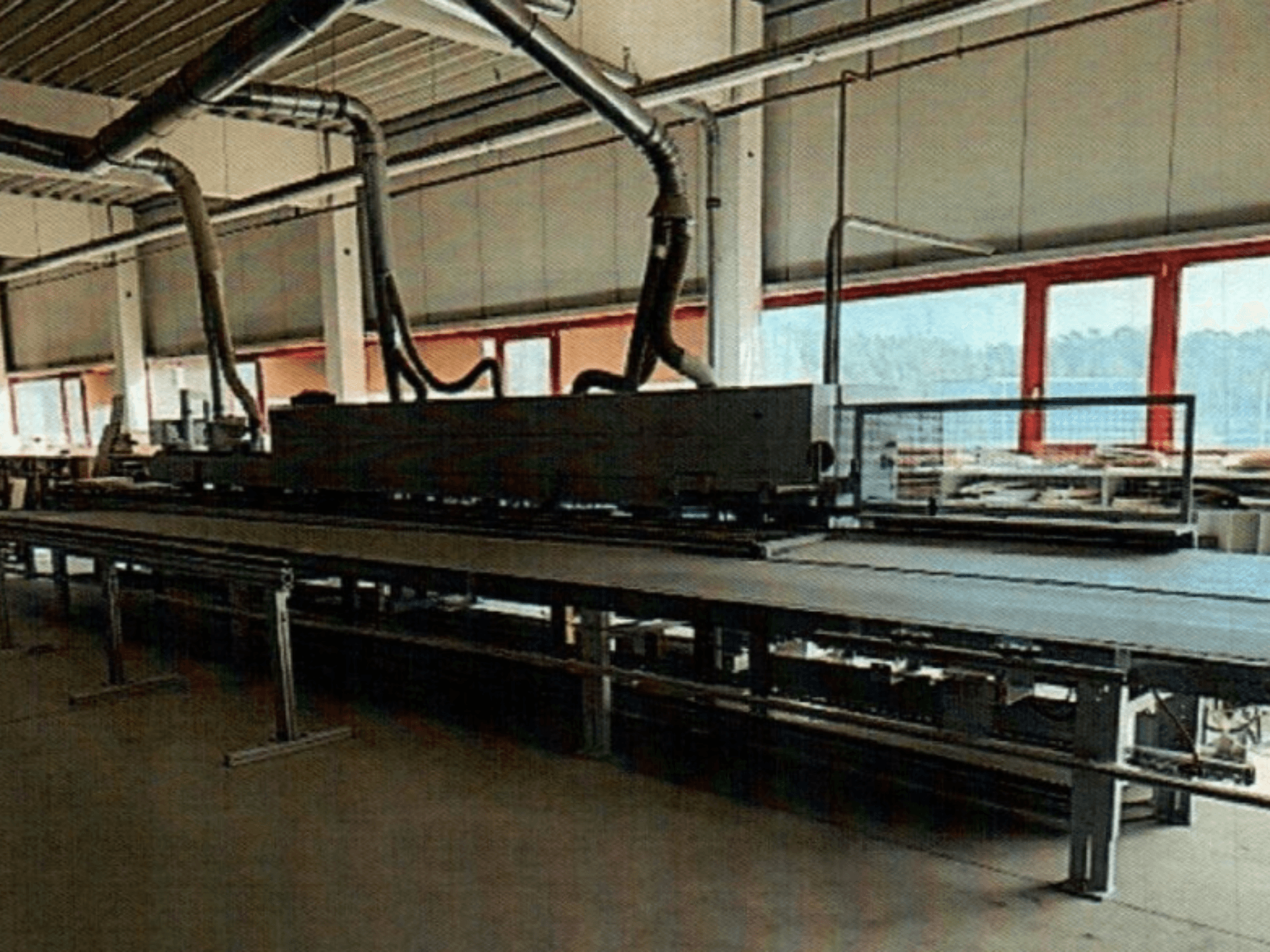 A coladeira de bordos HOMAG KAL 370 numa oficina, vista lateral, mostrando a mesa de trabalho longa e plana com condutas de ventilação por cima.