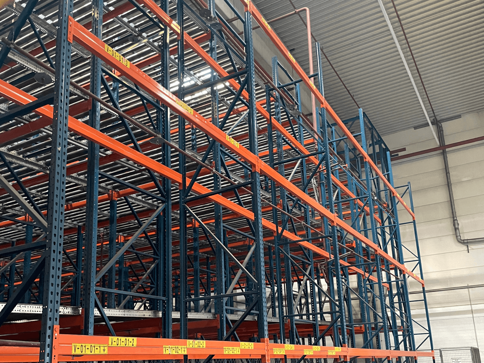 FL SYSTEME F05.10 Sistema de manuseamento de paletes FLG num armazém, visto de lado, com estantes resistentes de cor laranja e azul.