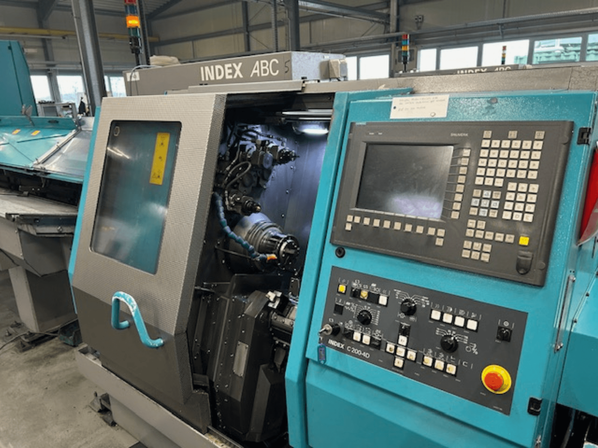 Vista frontal de um torno CNC INDEX C200-AD com painel de controlo, componentes internos visíveis e caraterísticas de segurança.