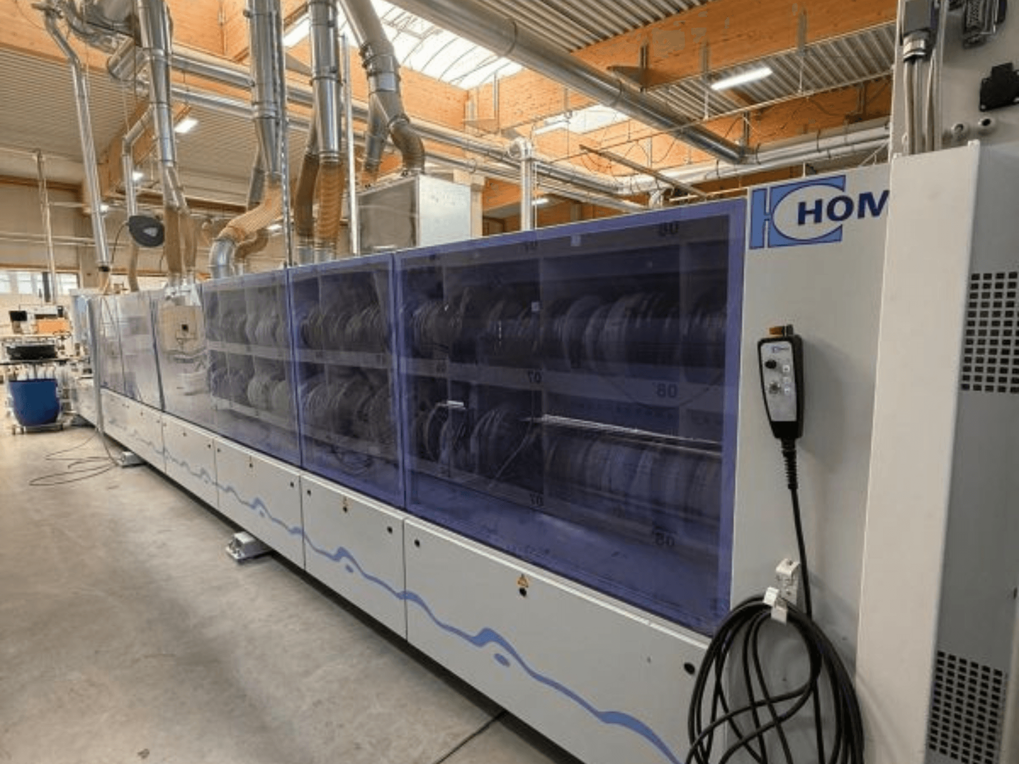 Máquina de lavar roupa industrial HOM, vista frontal, com painel transparente que exibe a loiça; painel de controlo com botões na lateral.