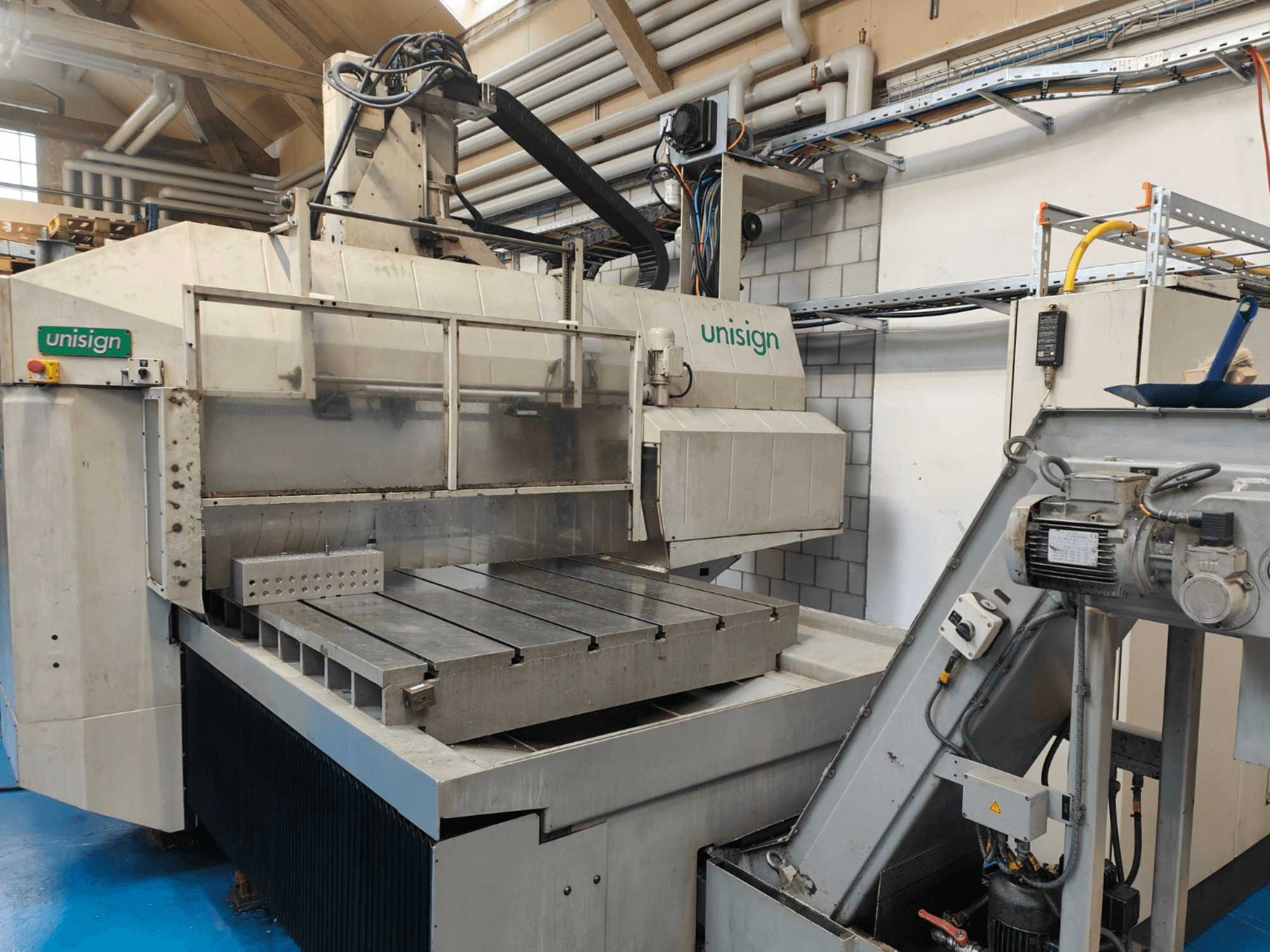 Máquina CNC Unisign numa oficina, vista frontal, com uma mesa grande, painel de controlo e elementos de design industrial.