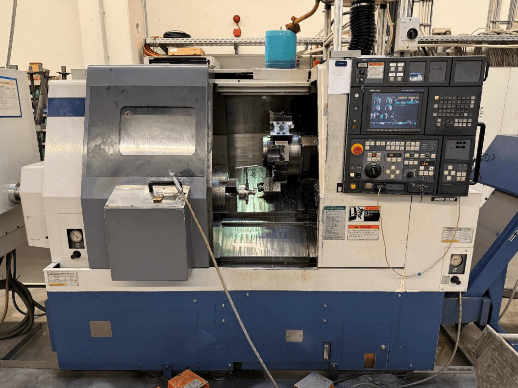 Centro de torneamento e fresagem MORI SEIKI SL-250ASMC, vista frontal que mostra o painel de controlo e o mandril da peça em funcionamento.