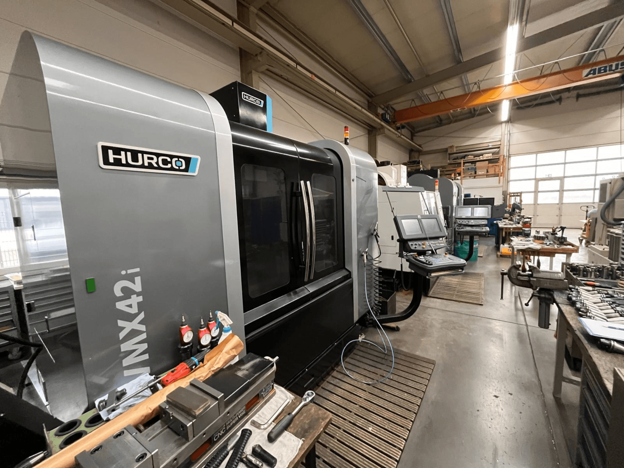 Máquina CNC Hurco VMX42i numa oficina, vista frontal. Apresenta painel de controlo, corpo cinzento e ambiente industrial.