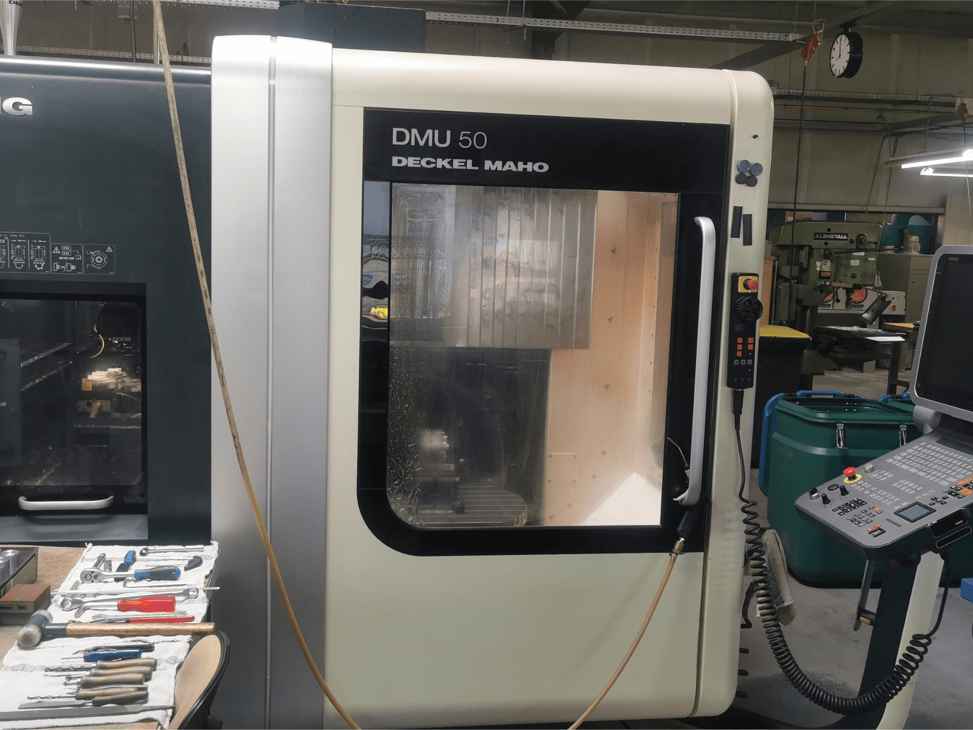 Máquina CNC DMU 50 deckel maho vista de frente, mostrando o painel de controlo e a porta transparente. As ferramentas estão próximas.