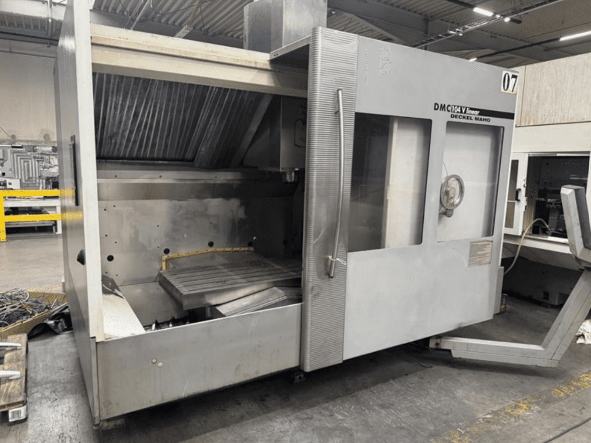 Máquina linear DMC 104 V da Deckel Maho, vista frontal, apresentando uma área de maquinação vazia com uma grande mesa de trabalho.