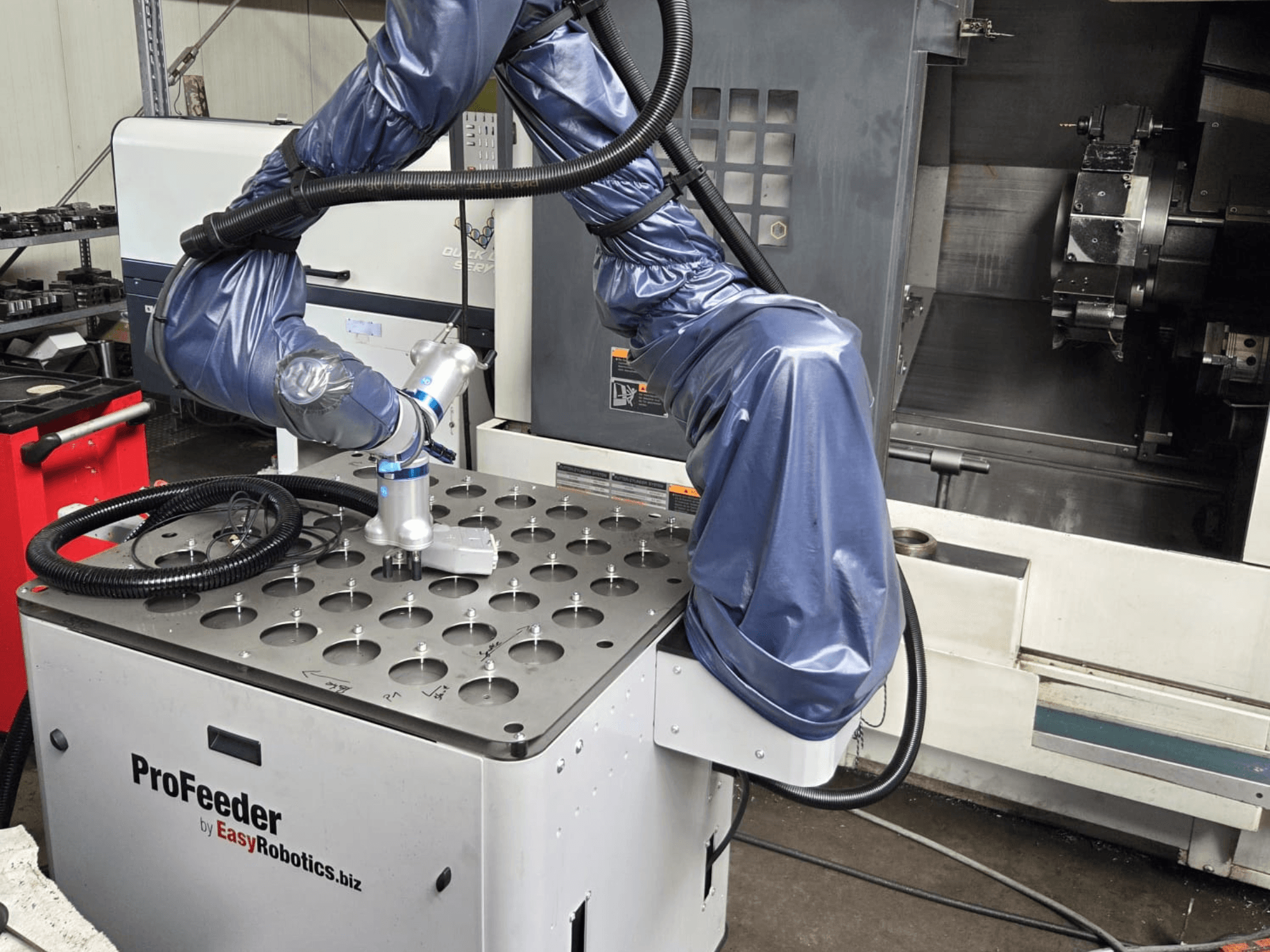 Robô colaborativo EASYROBOTICS ProFeeder numa vista frontal, com um braço robótico posicionado sobre uma mesa metálica perfurada.