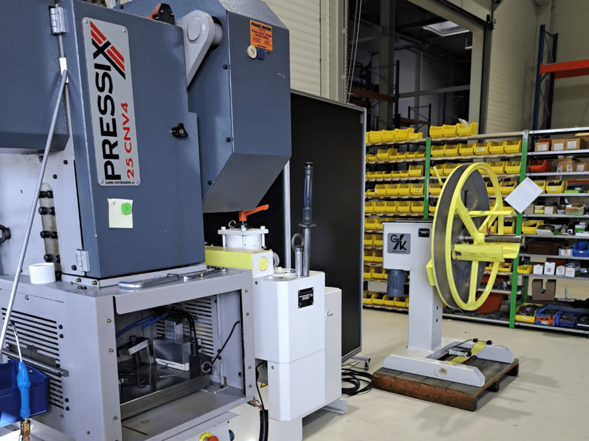 Configuração de máquina industrial com PRESSIX 25 CNV4 à esquerda e uma roda amarela montada numa base cinzenta à direita, vista frontal.