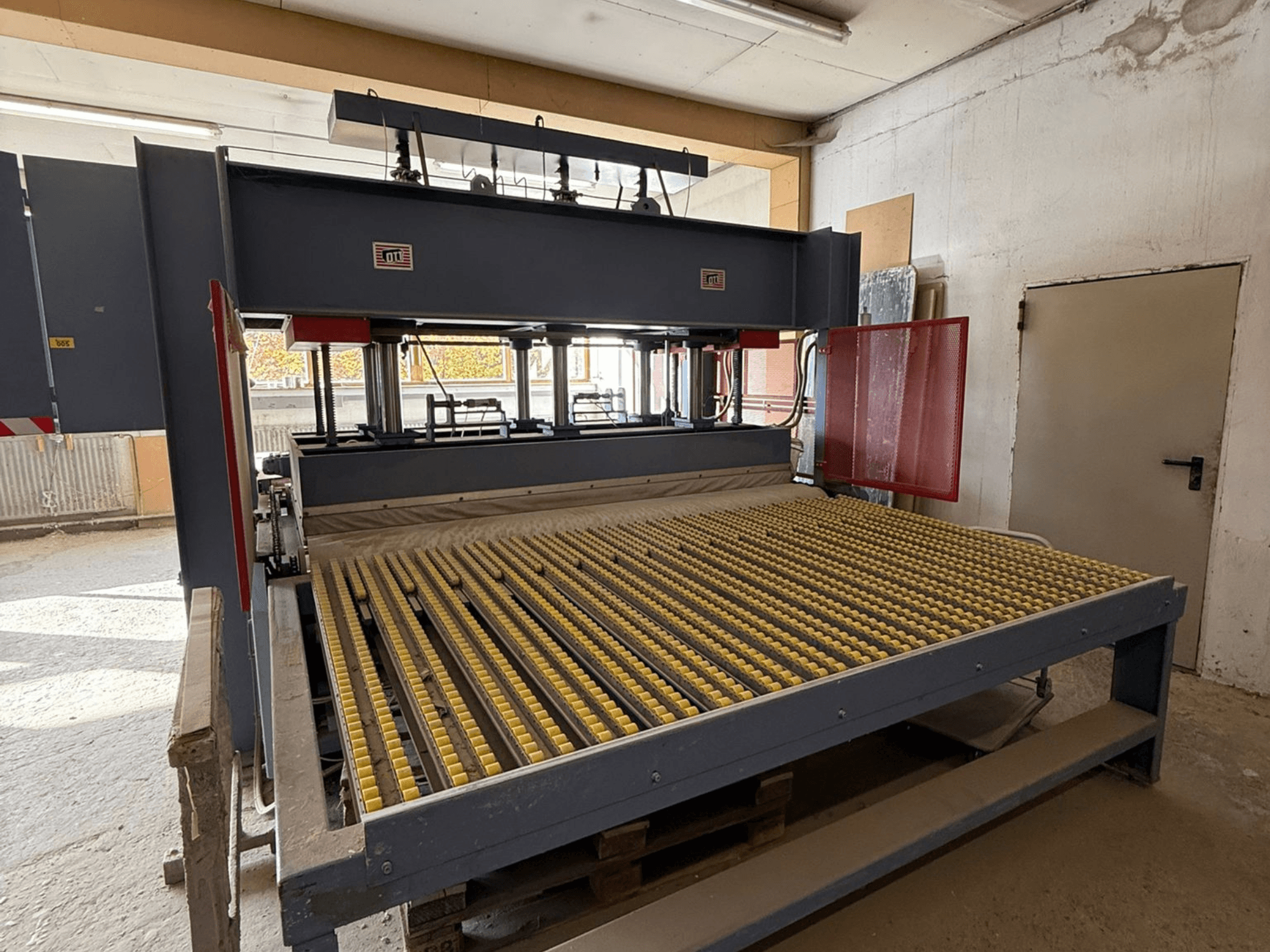 Máquina industrial com rolos amarelos, vista frontal, logótipo da marca visível, utilizada para processar materiais numa oficina.