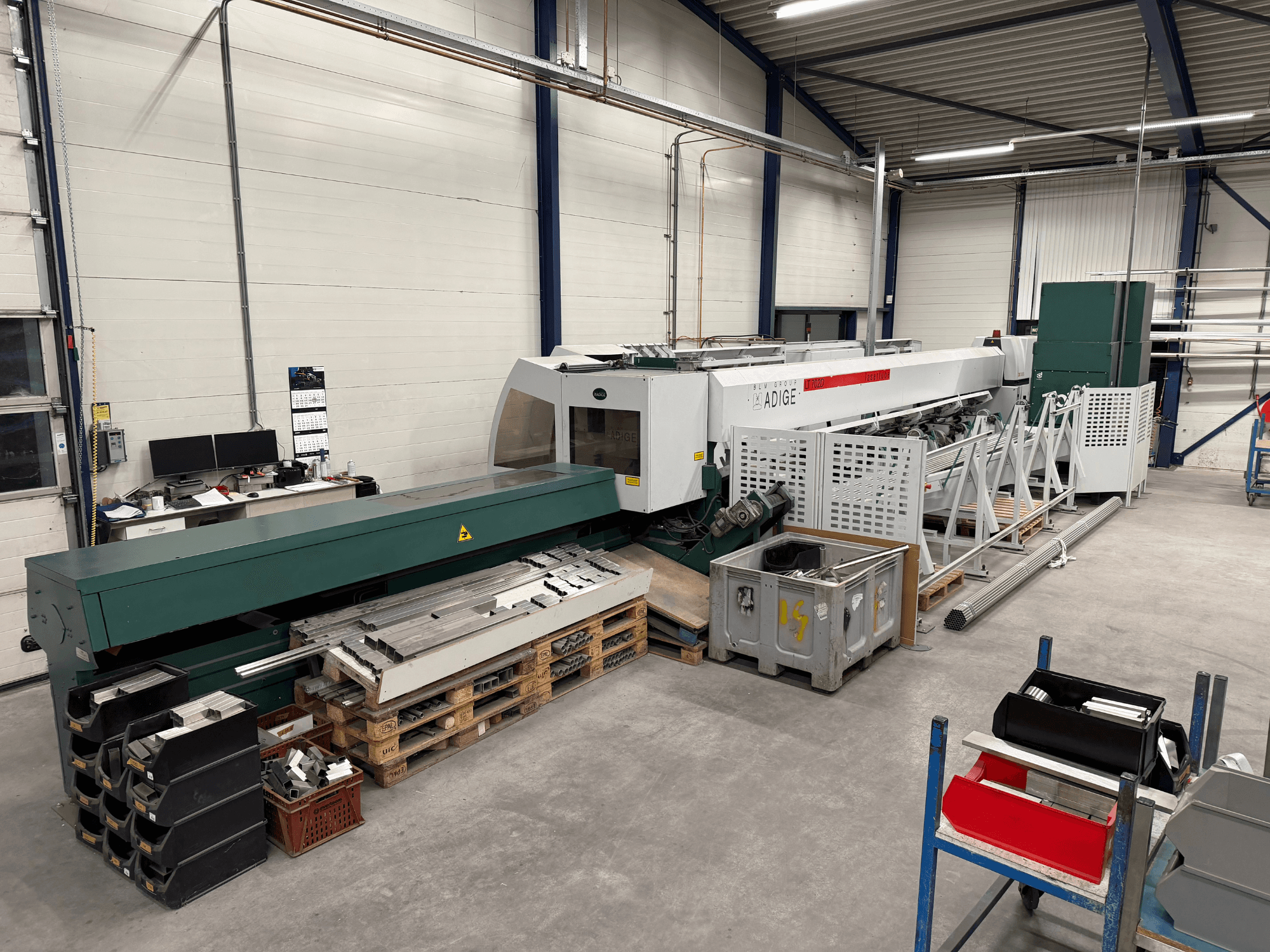 Máquina de corte a laser de CO₂ BLM Adige LT702 numa oficina, vista lateral com componentes metálicos e desordem na área de trabalho visíveis.