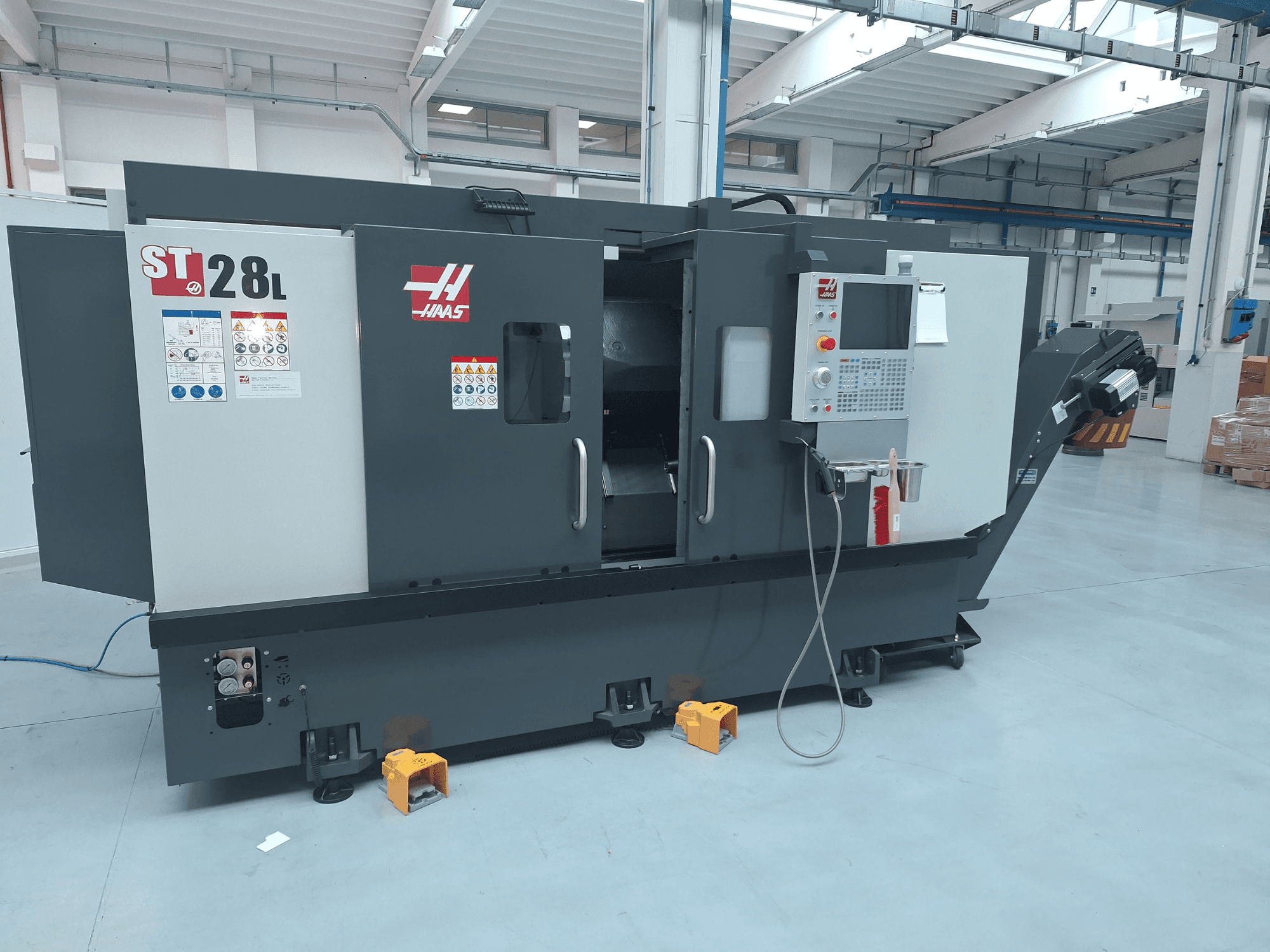 Vista lateral do torno horizontal Haas ST-28L, mostrando o painel de controlo, os botões operacionais e as etiquetas de segurança.
