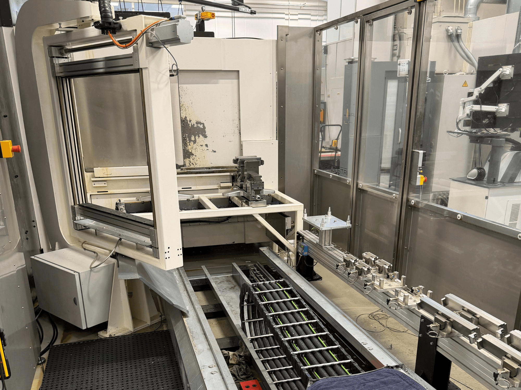 Estação de trabalho industrial automatizada com um braço robótico, sistema de calhas e painel de controlo numa vista lateral.