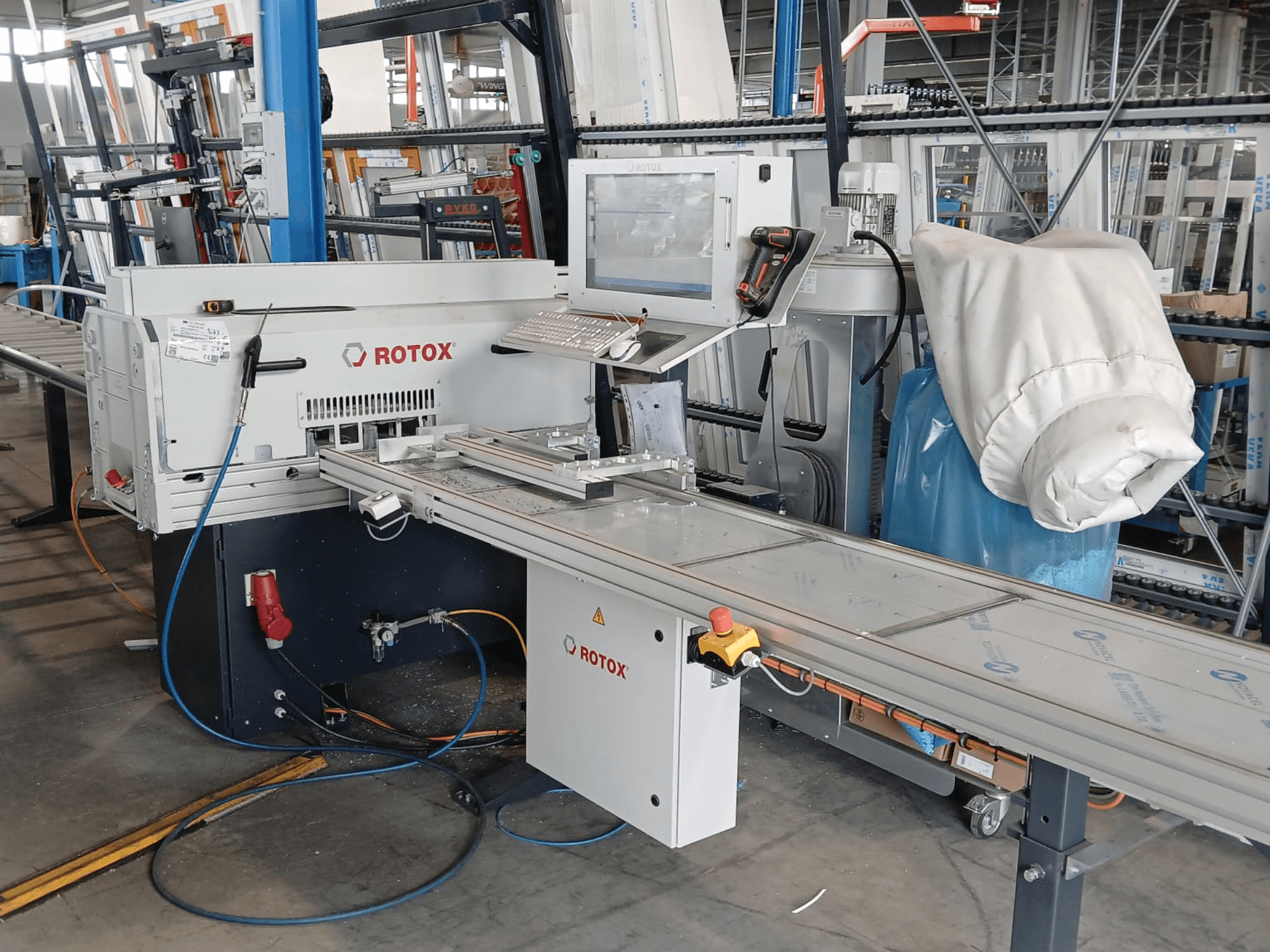 Vista frontal de uma máquina de processamento de plástico Rotox GLA401 com painel de controlo, transportador e mangueiras visíveis num ambiente industrial.