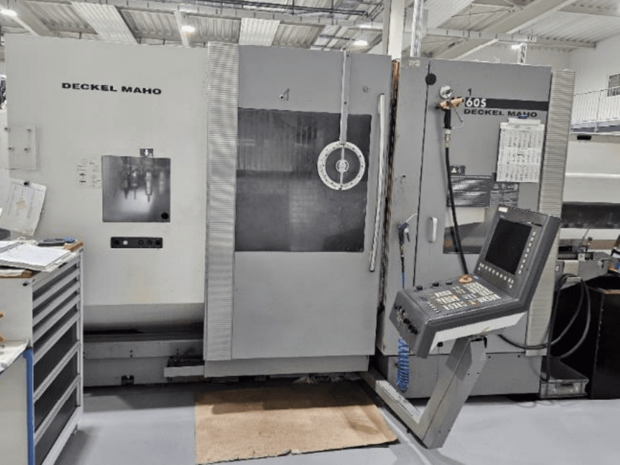 Vista frontal de uma máquina CNC DECKEL MAHO 60S com painel de controlo, ferramentas visíveis, numa oficina.