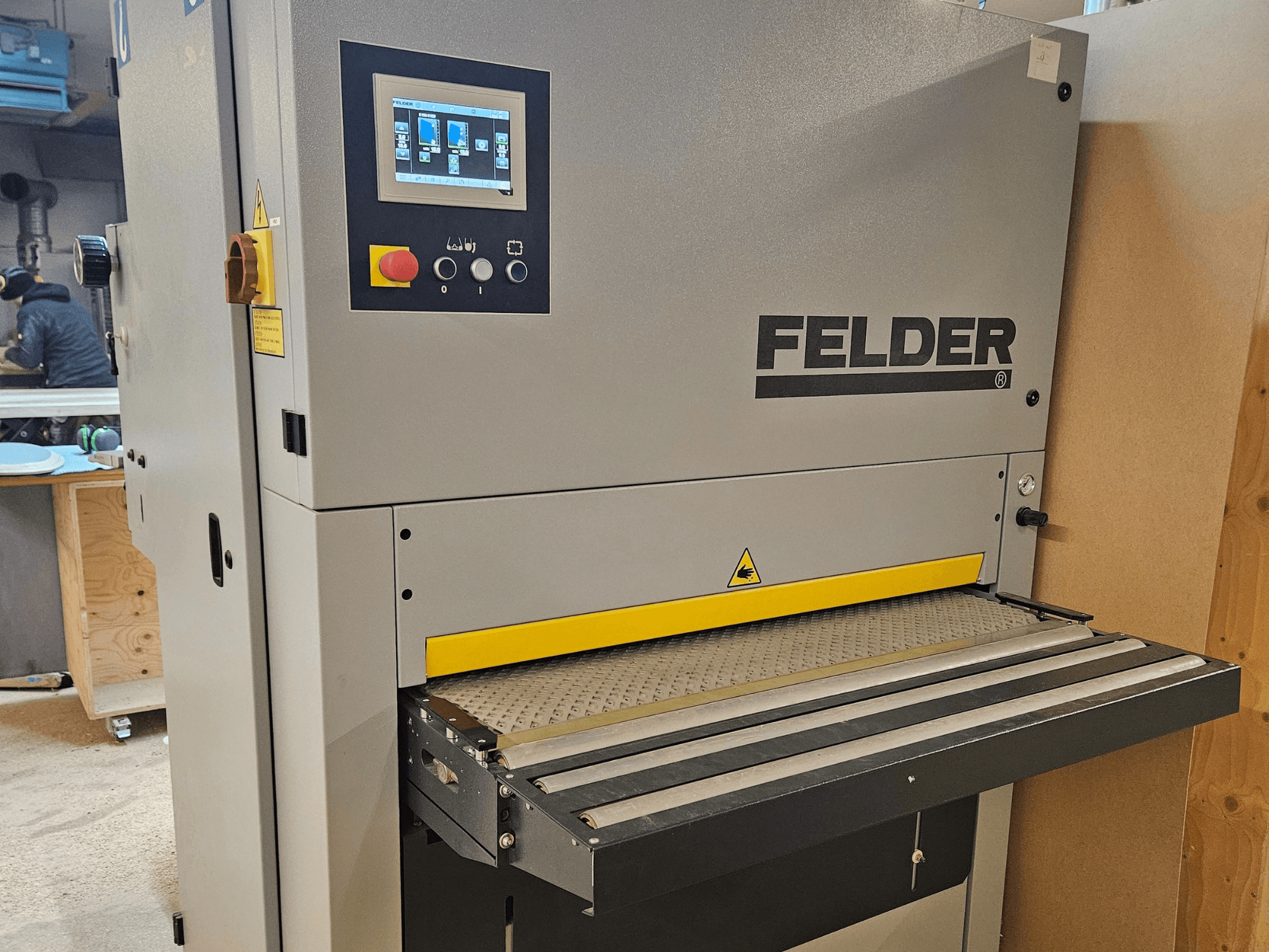 Máquina para trabalhar madeira FELDER em vista frontal, com painel de controlo digital e mesa de alimentação amarela com avisos de segurança.