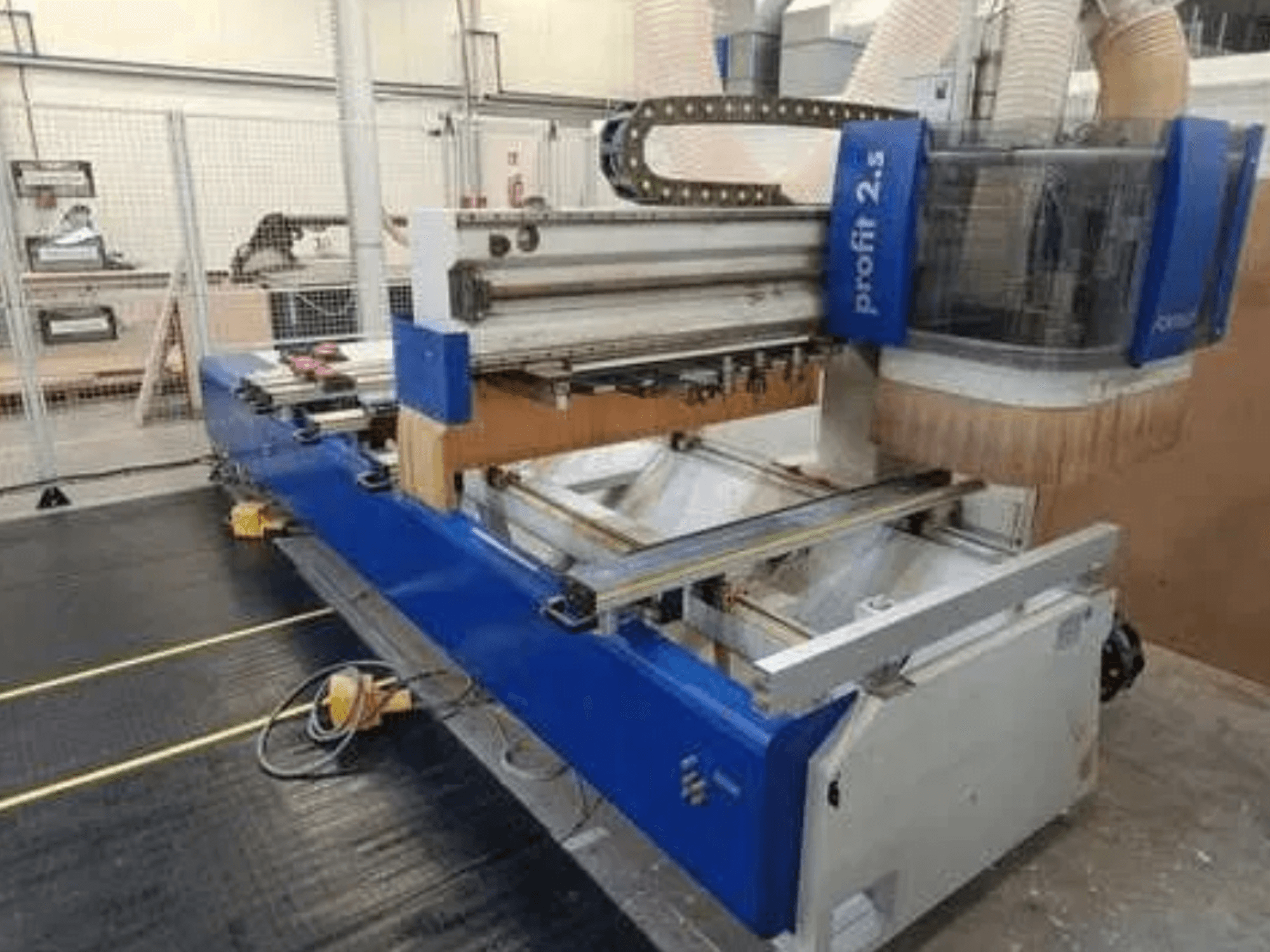 Máquina CNC, marca Profitec 2.5, a vista frontal mostra o corpo azul, a área de trabalho e o bocal de extração de poeiras para processamento de madeira.