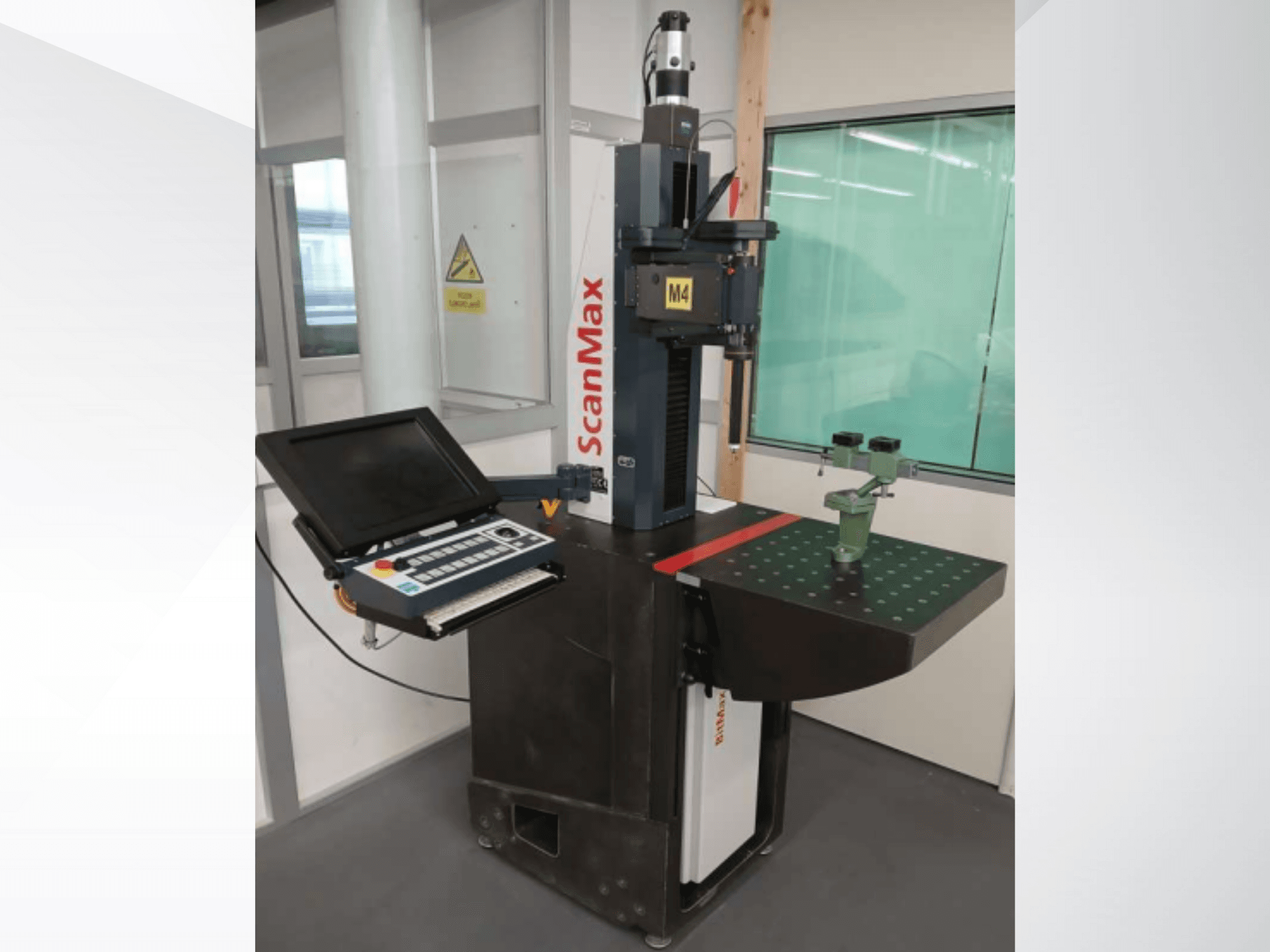 Máquina de medição ScanMax M4, vista frontal com painel de controlo e dispositivo de calibração verde numa mesa de trabalho pontilhada.