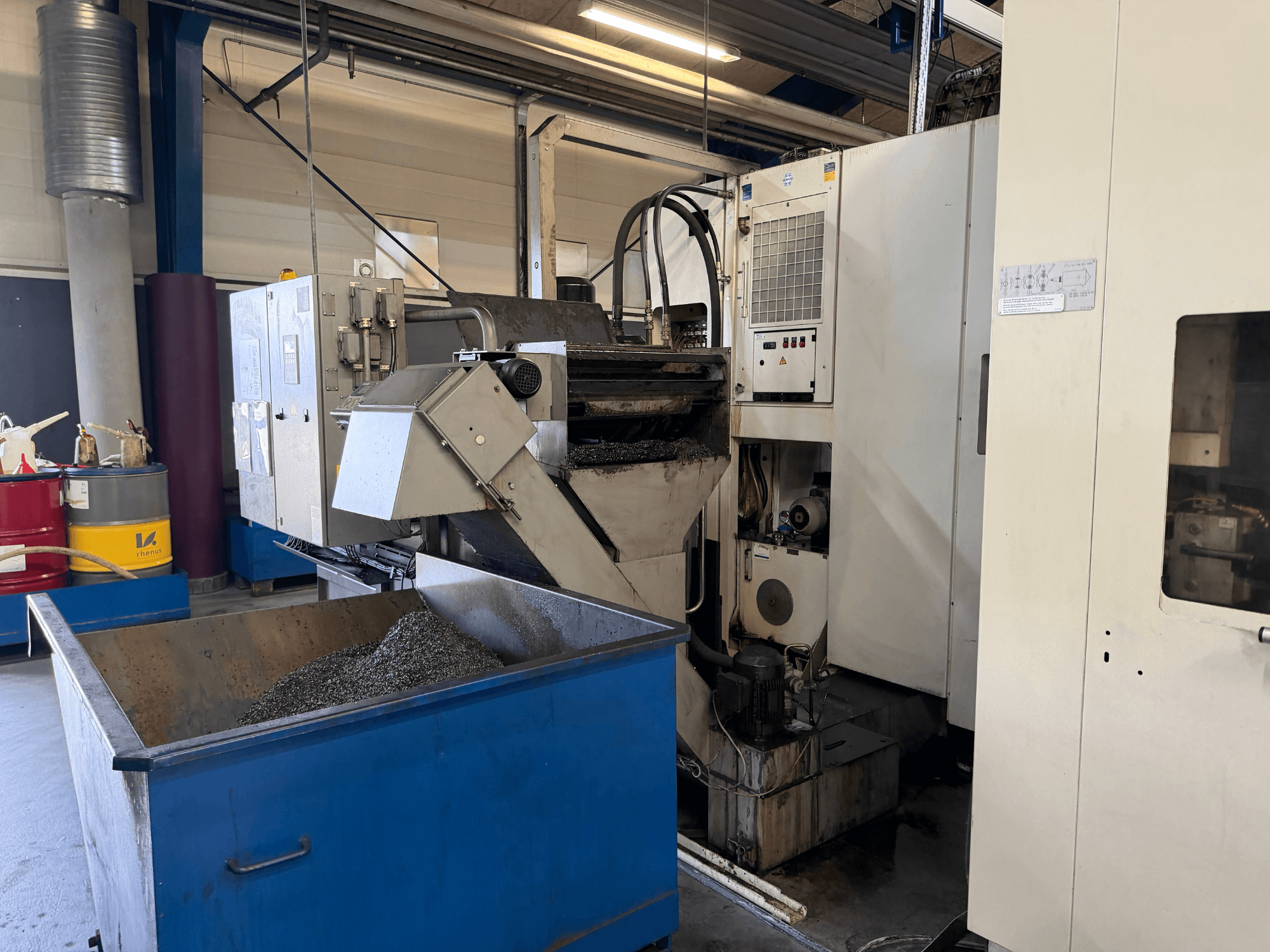 Vista frontal do centro de maquinação horizontal HELLER MCH 250 com o depósito de reciclagem de metal refrigerante e o painel de controlo visíveis.