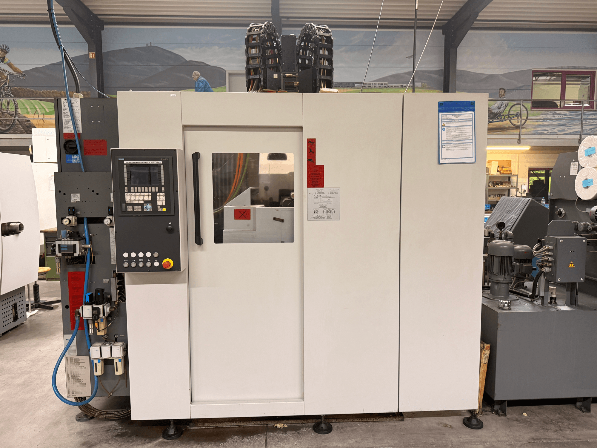 Centro de maquinação CNC branco com painel de controlo, vista frontal, com botões e visor digital, numa oficina.