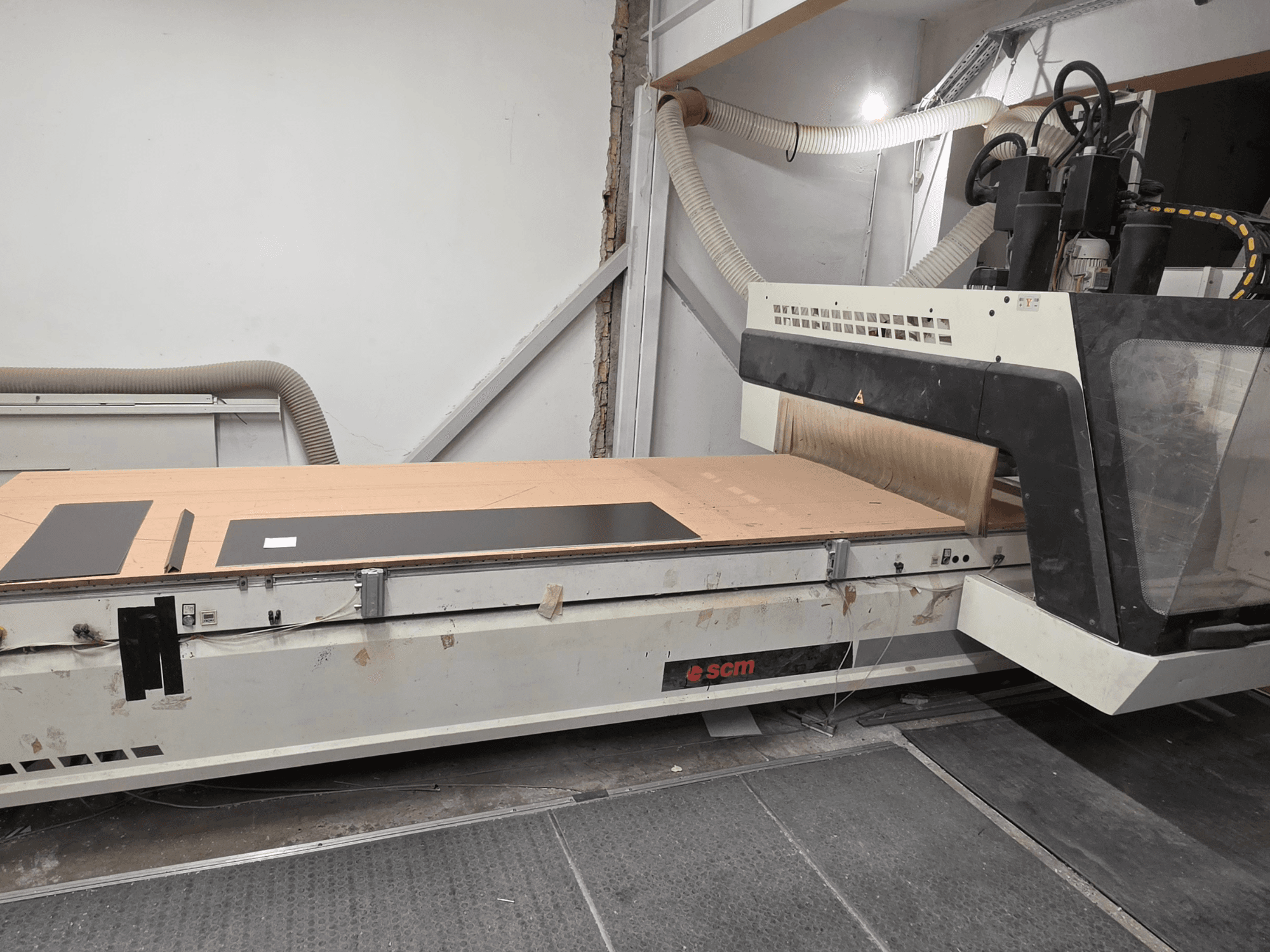 Centro de usinagem de madeira CNC SCM RECORD 132, visto de perfil, com uma mesa de trabalho plana, peças de trabalho pretas e sistema de recolha de poeira.