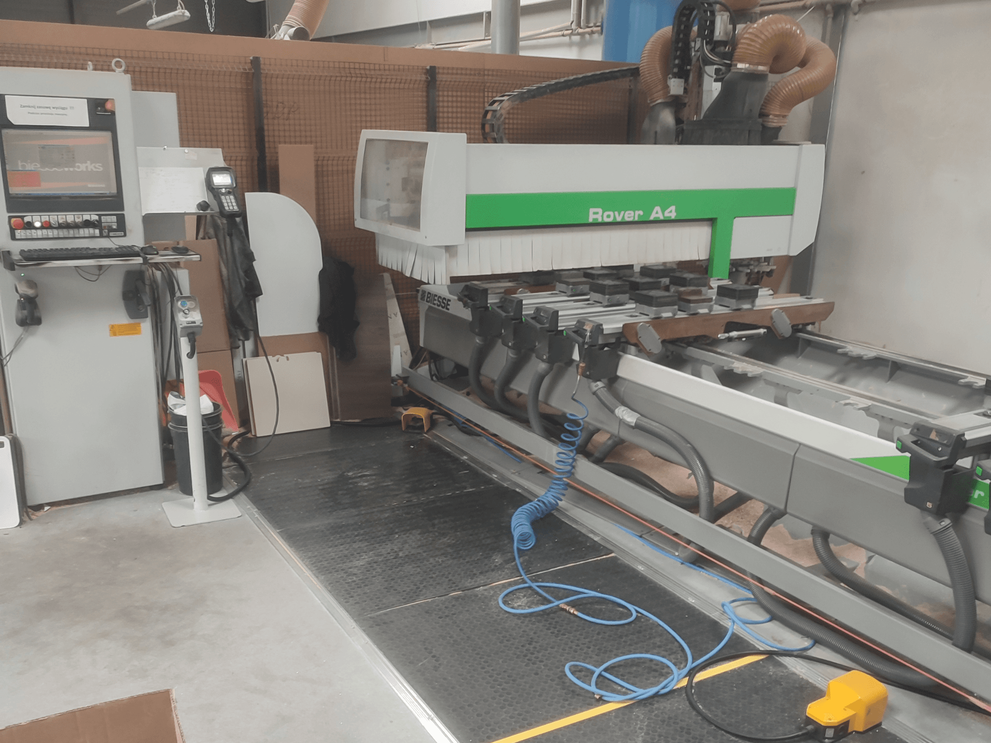 Centro de usinagem de madeira BIESSE Rover A4 CNC, visto de lado, mostrando o painel de controlo, os dispositivos de fixação a vácuo e o sistema de extração de poeira.