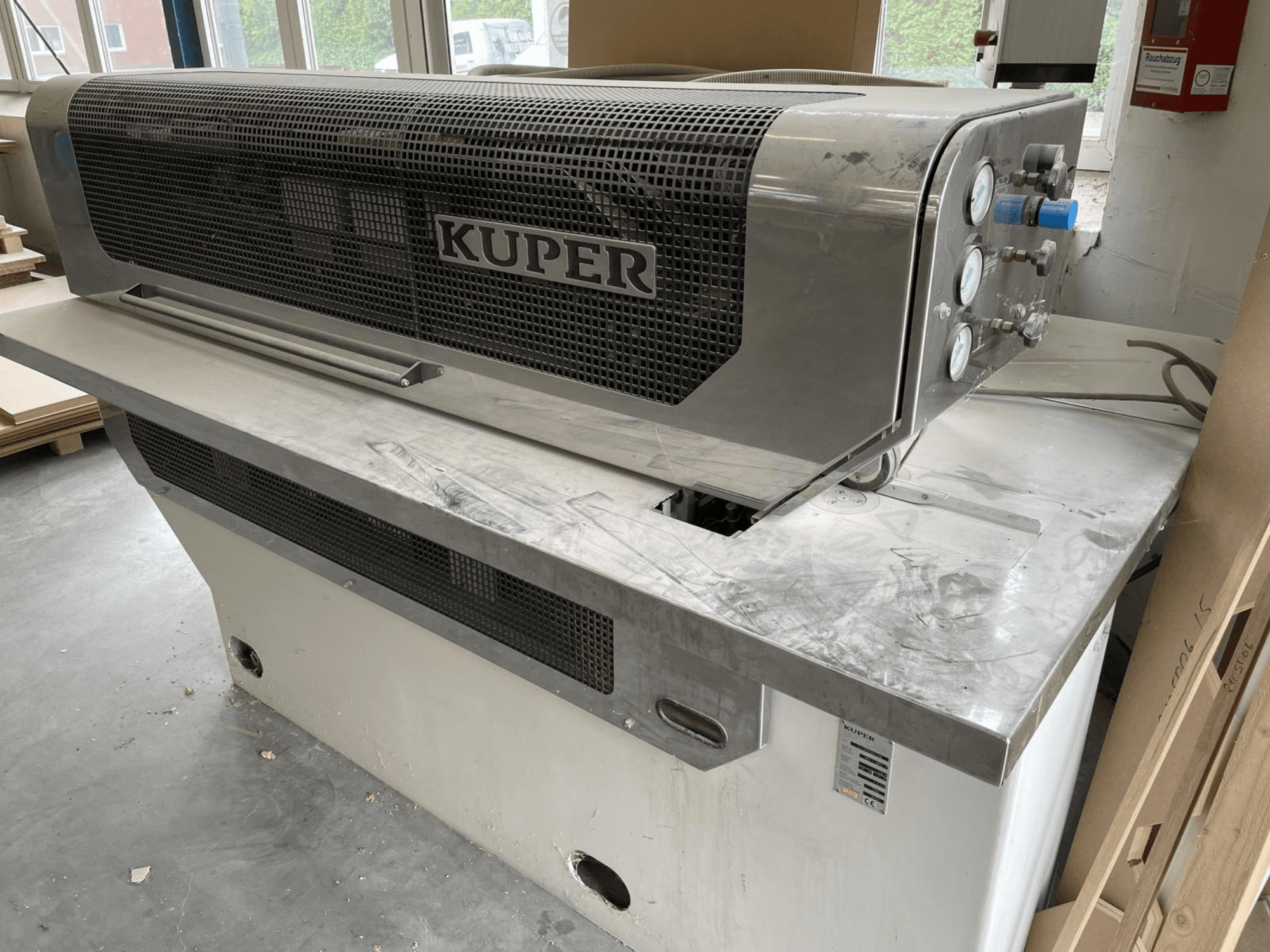 Guilhotina para folheados KUPER FLI, vista frontal, com um corpo em aço inoxidável, manómetros e uma área de corte limpa numa bancada de trabalho.