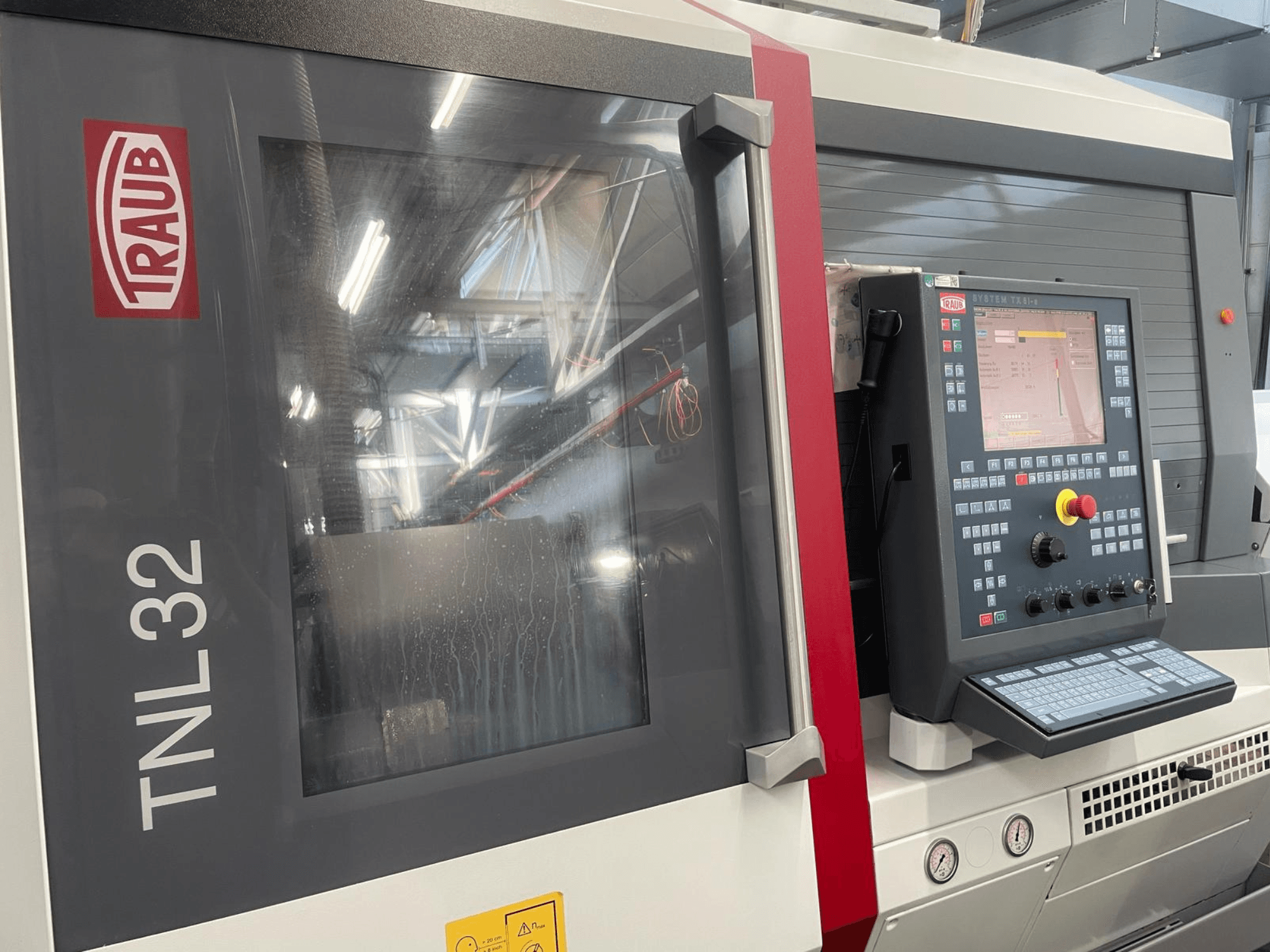 Vista frontal do torno CNC Traub TNL32, com painel de controlo com botões, ecrã de visualização e caixa metálica elegante.