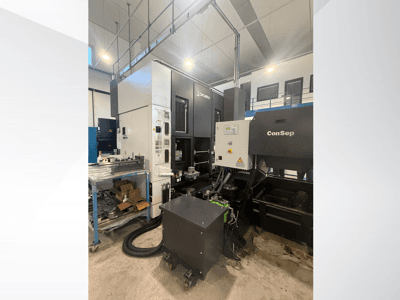 Centro de maquinação Okuma com unidade ConSep, vista lateral, mostrando os controlos e a configuração industrial, incluindo o depósito de aparas de metal.