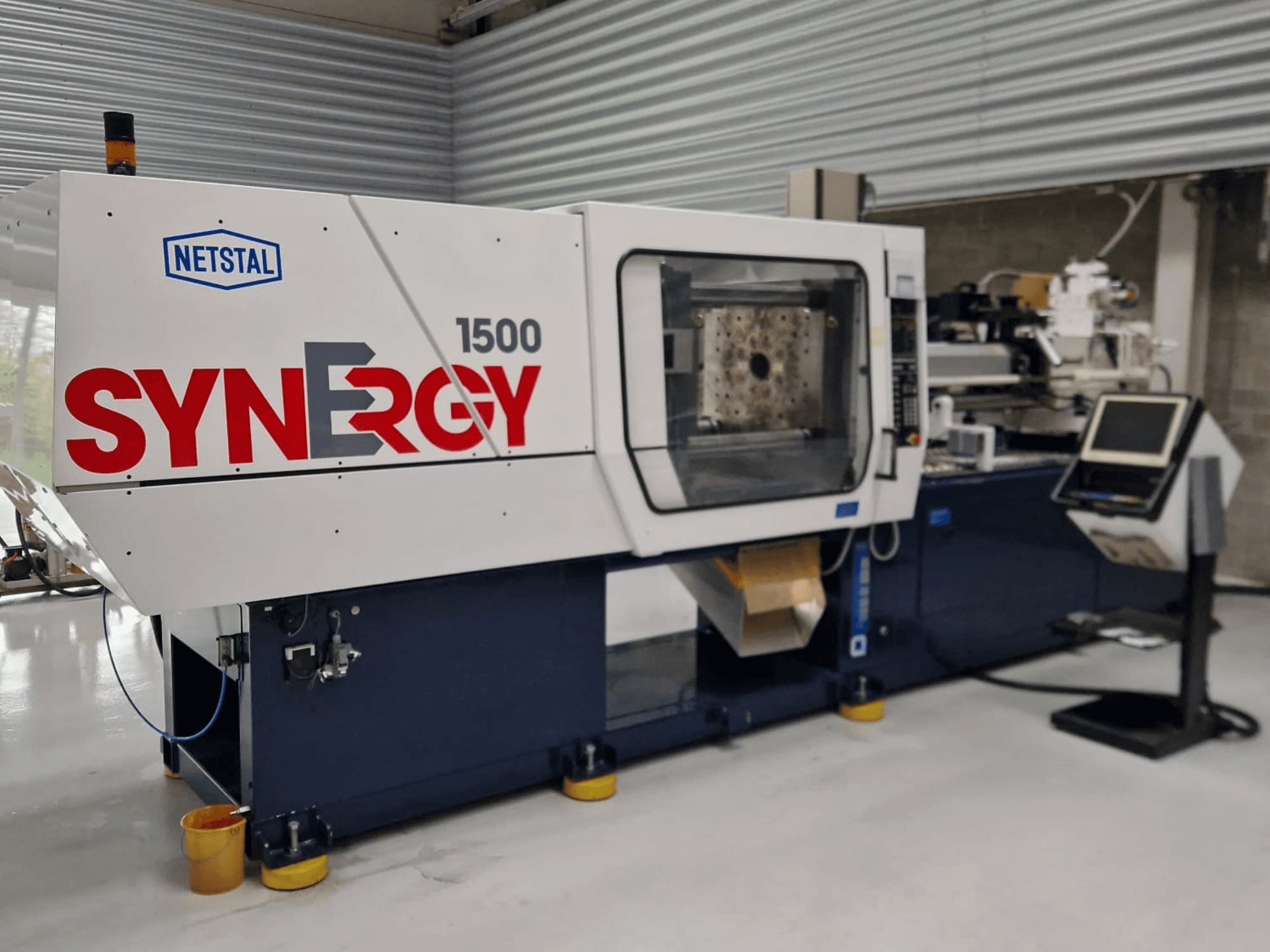 Máquina de moldagem por injeção hidráulica Netstal Synergy 1500-460, vista frontal, mostrando o painel de controlo e a área de injeção aberta.