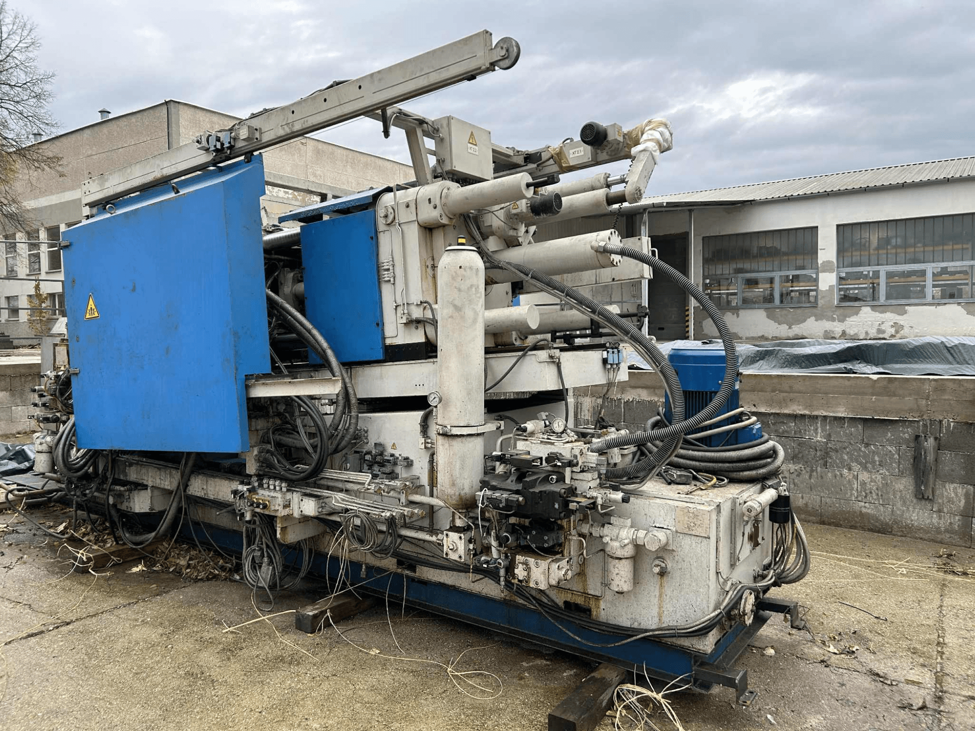 Grande máquina hidráulica industrial com caixa azul, várias mangueiras e componentes metálicos, vista de lado.