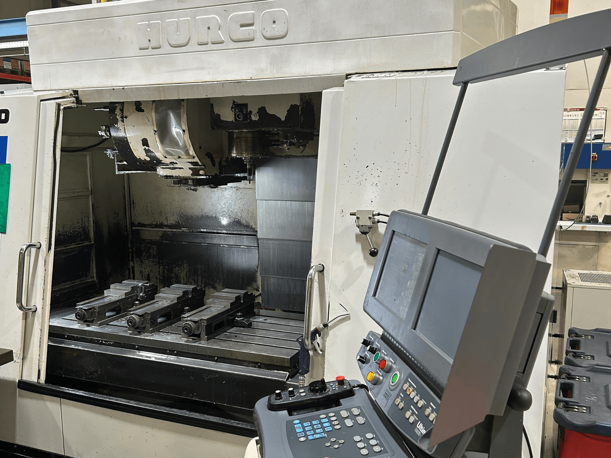 Fresadora CNC Hurco, vista frontal, com quatro suportes de ferramentas na mesa e um painel de controlo com dois ecrãs e botões.