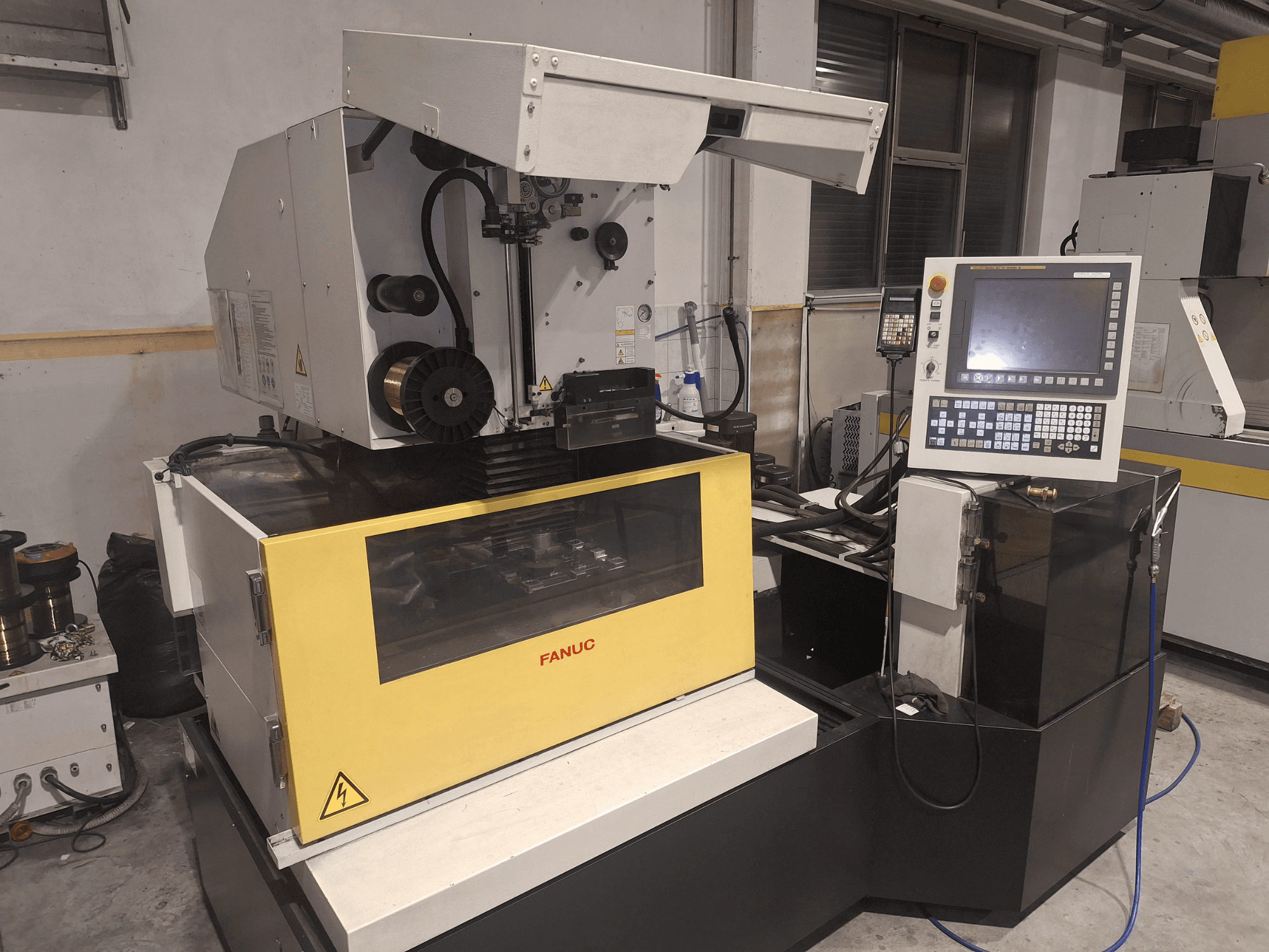 Máquina CNC FANUC em vista frontal com a tampa aberta, revelando a área de trabalho e o painel de controlo à direita.