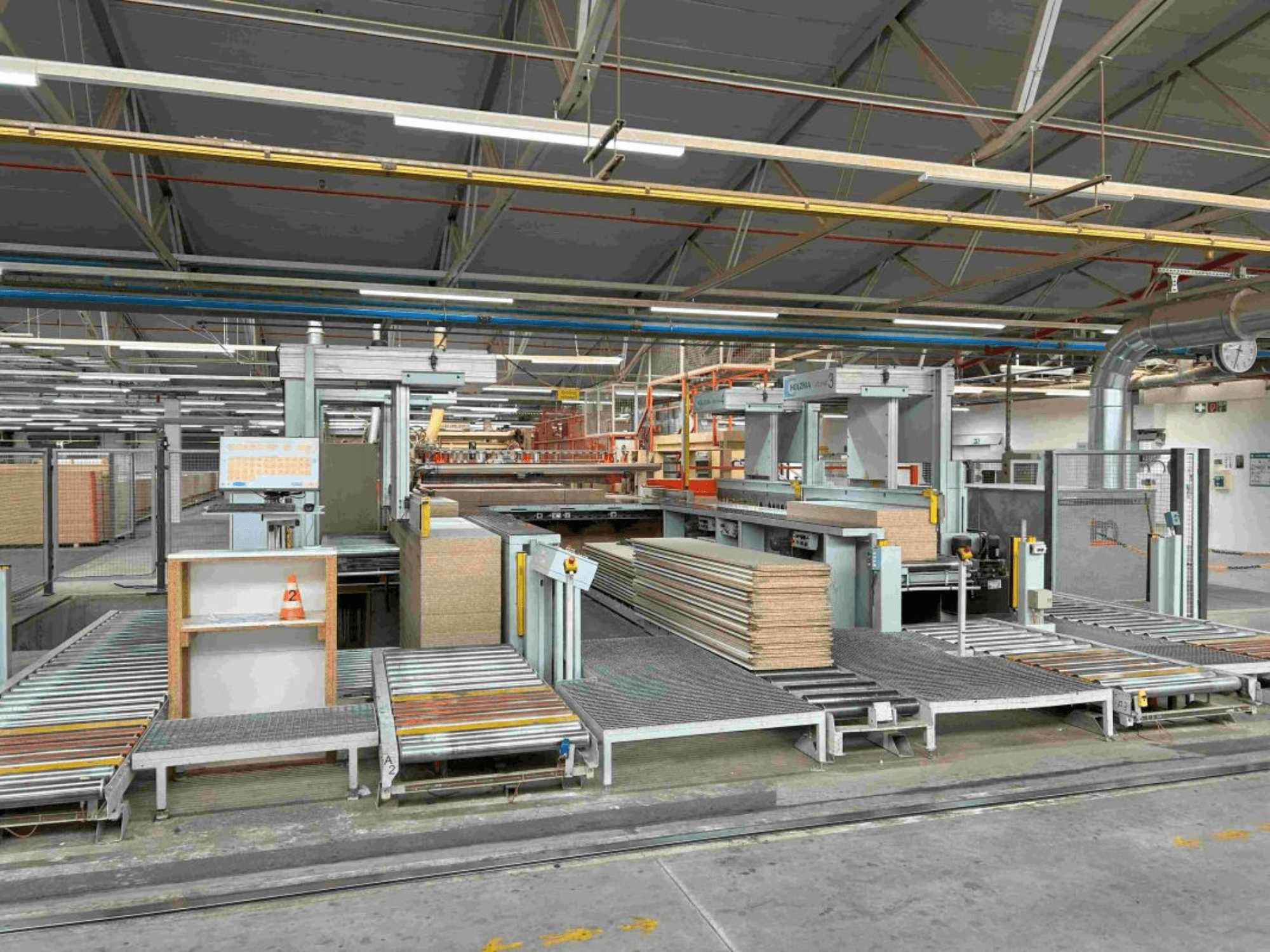 Interior de uma instalação de fabrico mostrando linhas de montagem com painéis empilhados e maquinaria, vista frontal, iluminação brilhante, equipamento moderno.
