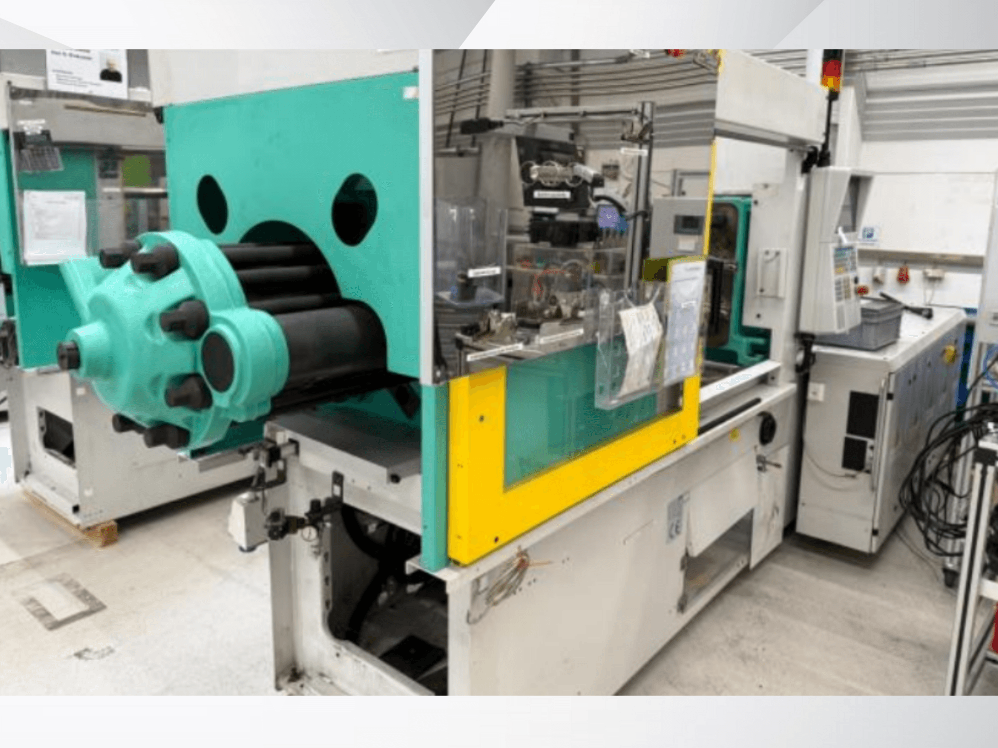 Máquina de moldagem por injeção, azul claro e amarelo, vista frontal, com um molde visível e um painel de controlo com etiquetas.