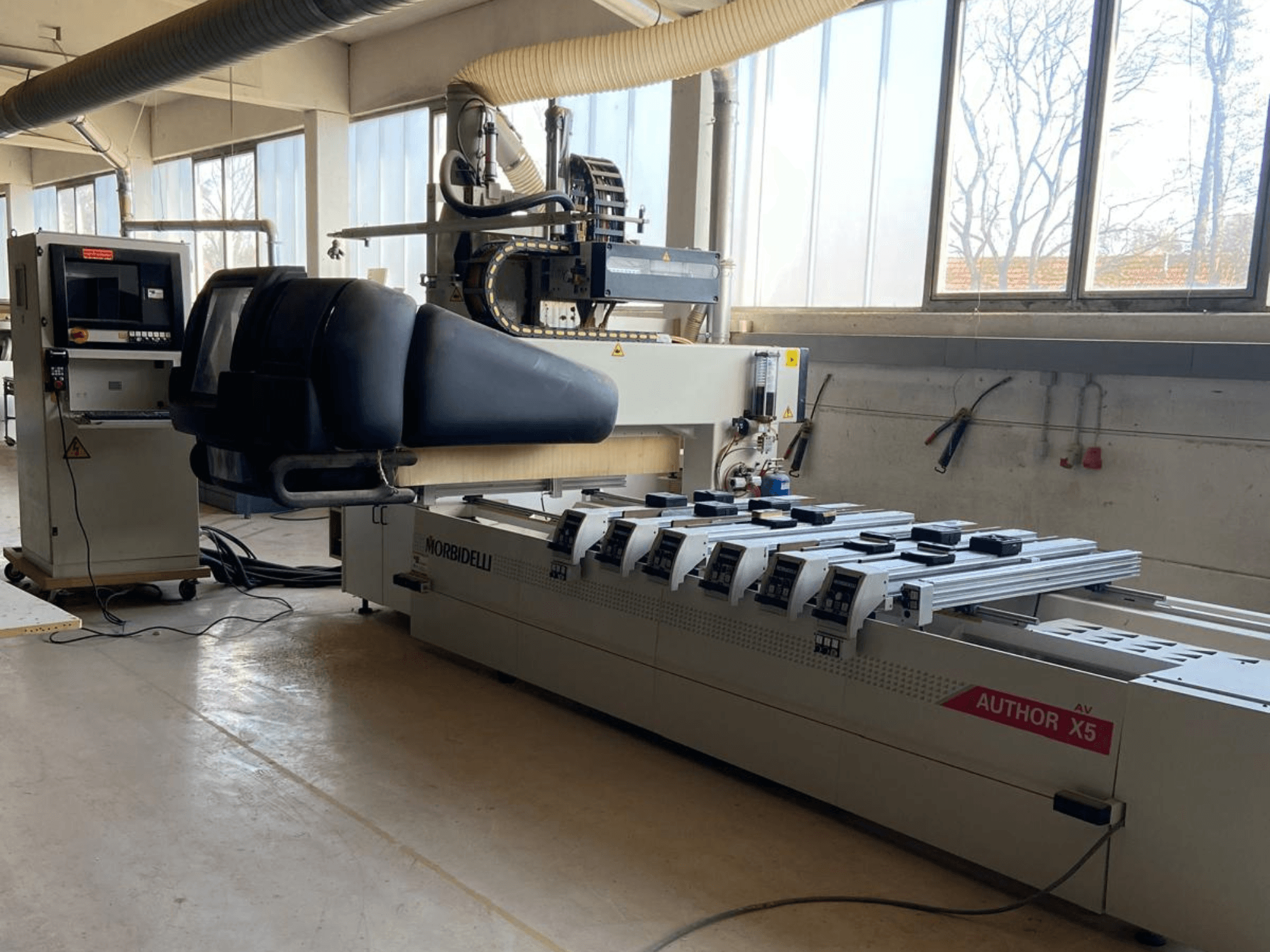 Centro de maquinação CNC para madeira MORBIDELLI Author X5 numa oficina, mostrando o painel de controlo e a área de maquinação a partir de uma vista lateral.