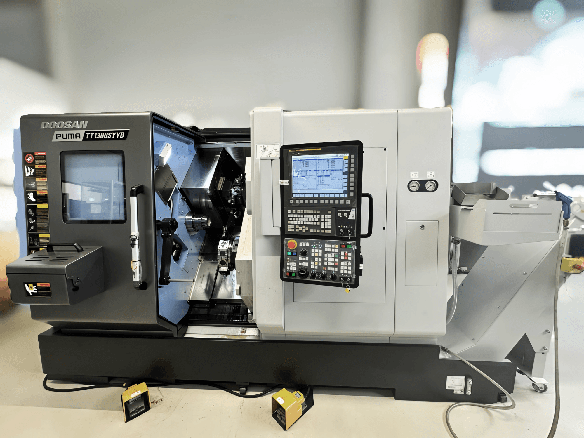 Centro de torneamento-fresagem Doosan Puma TT1300SYYB em vista lateral, mostrando o painel de controlo e o interior da máquina com ferramentas visíveis.