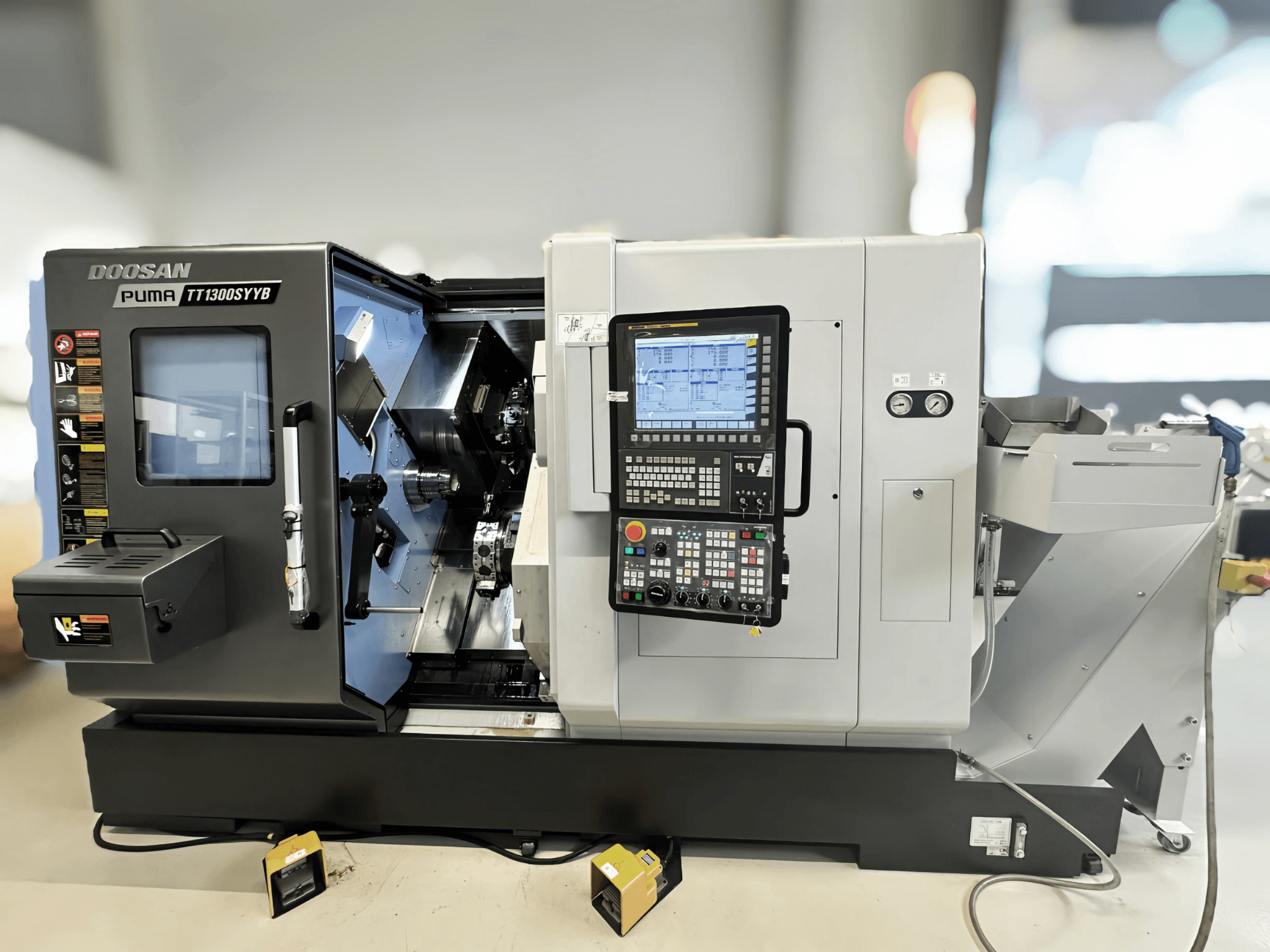 Centro de torneamento-fresagem Doosan Puma TT1300SYYB em vista lateral, mostrando o painel de controlo e o interior da máquina com ferramentas visíveis.