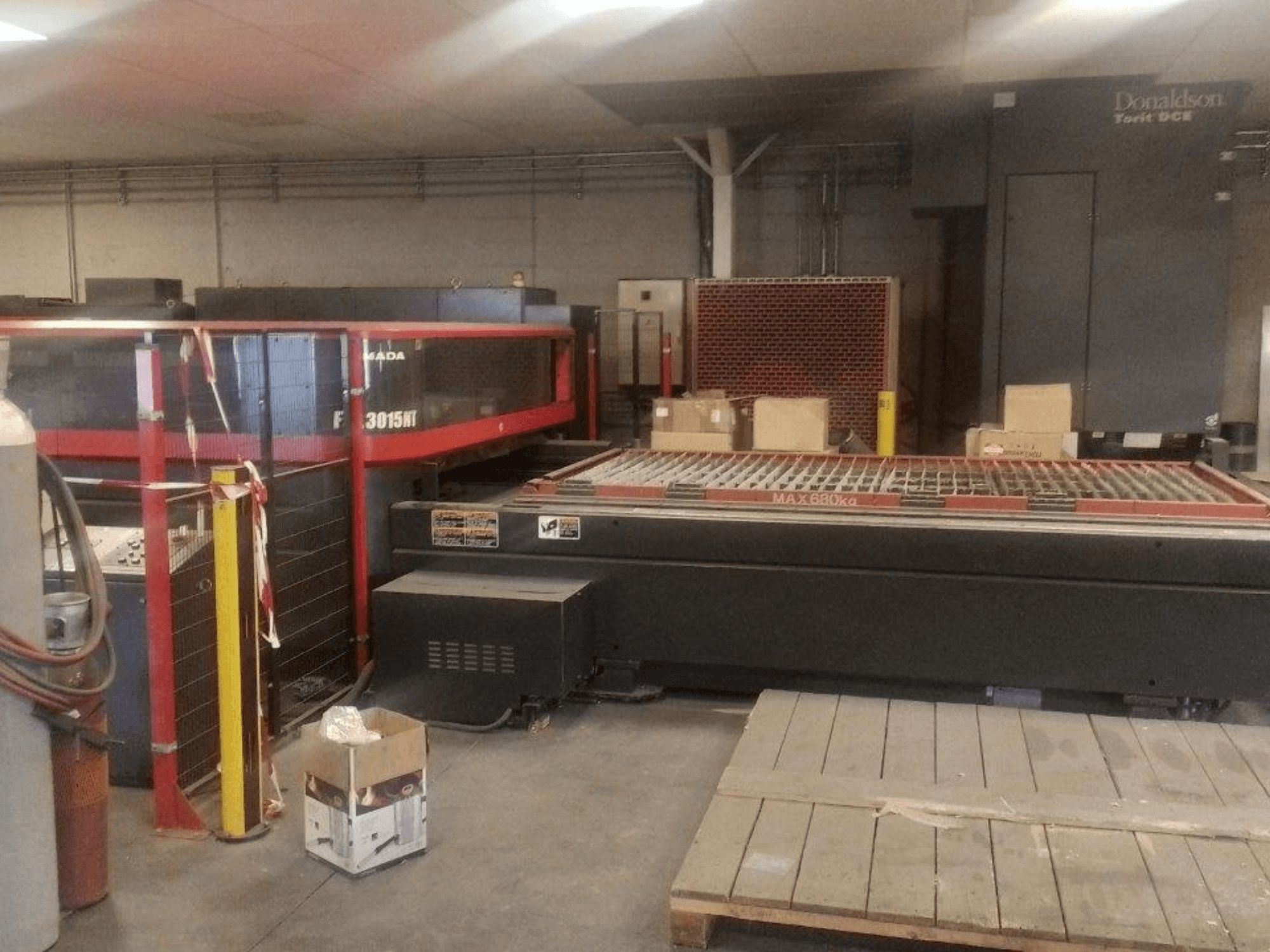 Máquina de corte a laser de CO₂ AMADA FOL 3015 NT, vista frontal; cabina de segurança vermelha, mesa de trabalho com grelha, ambiente industrial.
