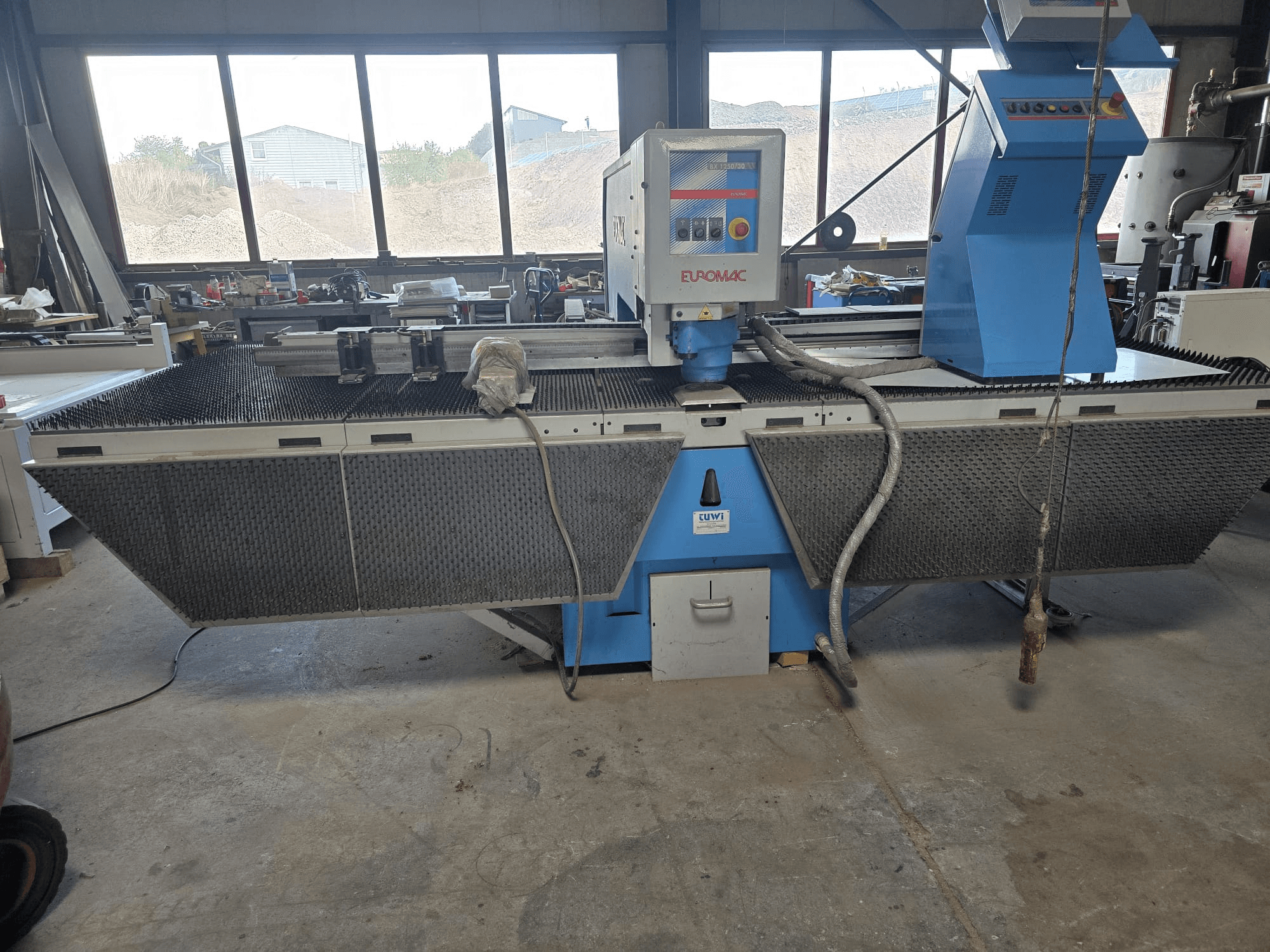Máquina de perfuração CNC Euromac BX 1250/30 numa oficina, vista lateral que mostra os comandos da máquina, o design industrial e a base de corte de metal.