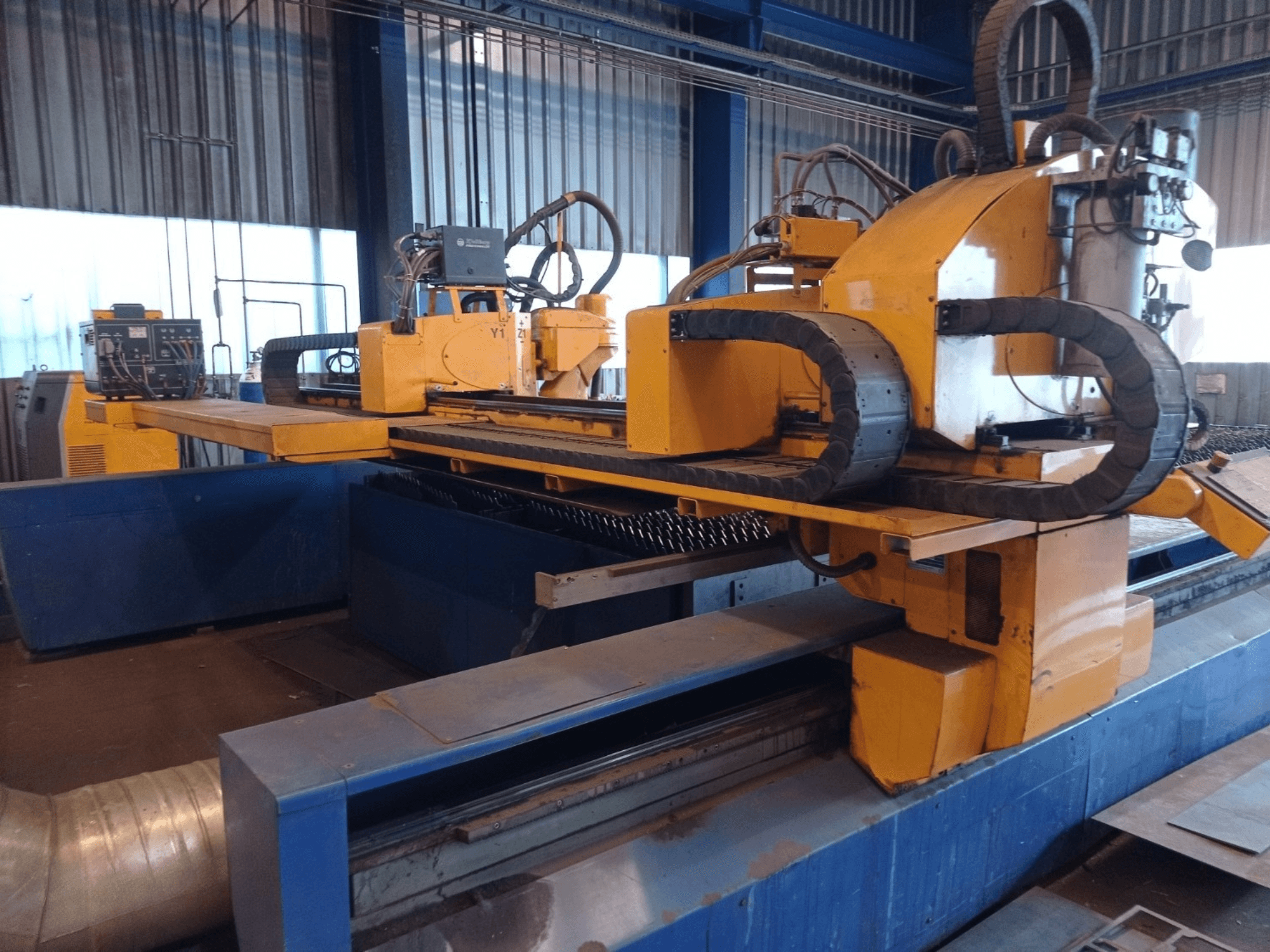 Máquina de corte por plasma CNC amarela com dois braços horizontais, vista de frente, com painel de controlo e base de corte.