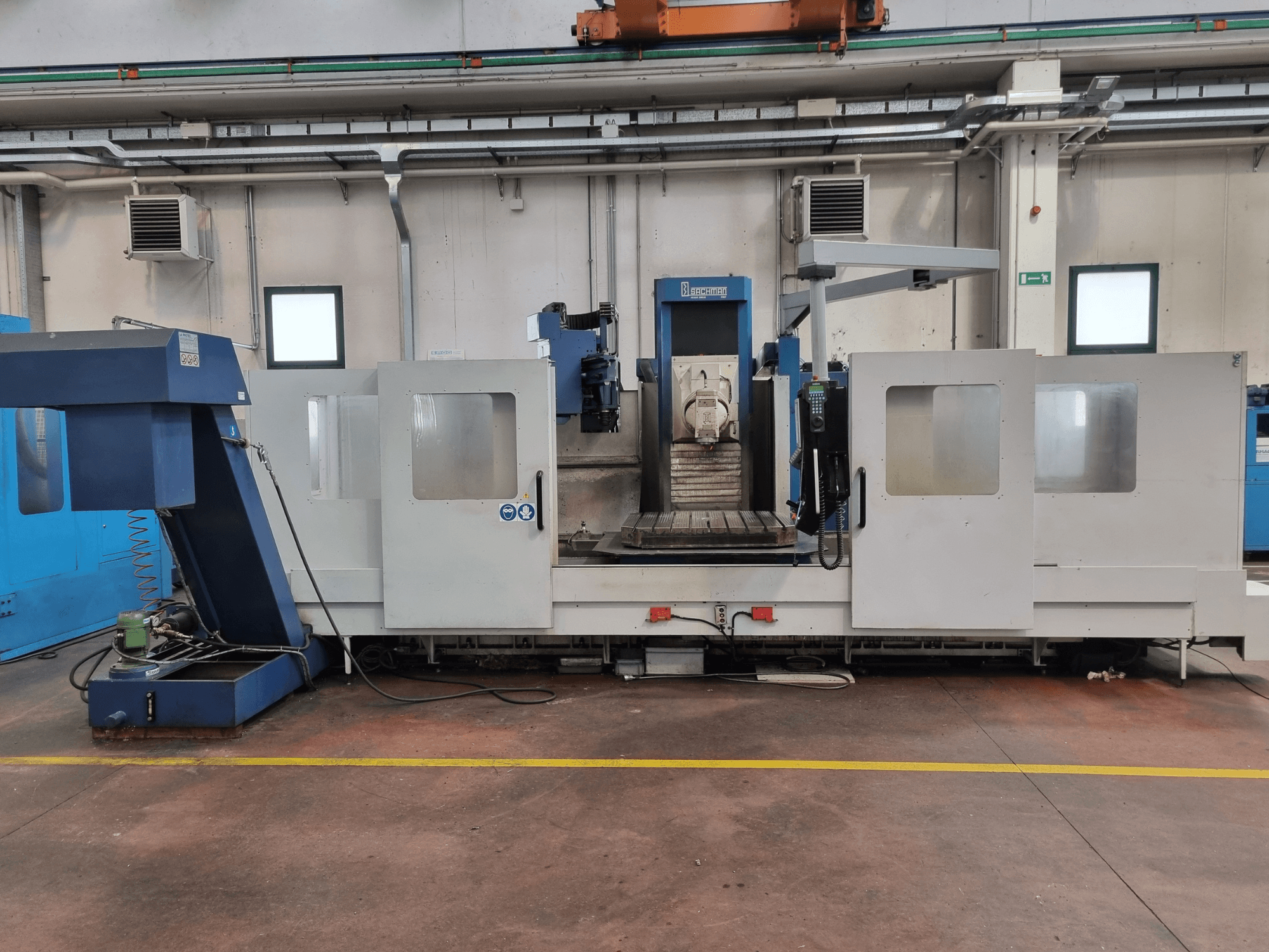 Fresadora CNC da "Brembana", vista lateral mostrando o painel de controlo e a área operacional com uma mesa de trabalho no interior.