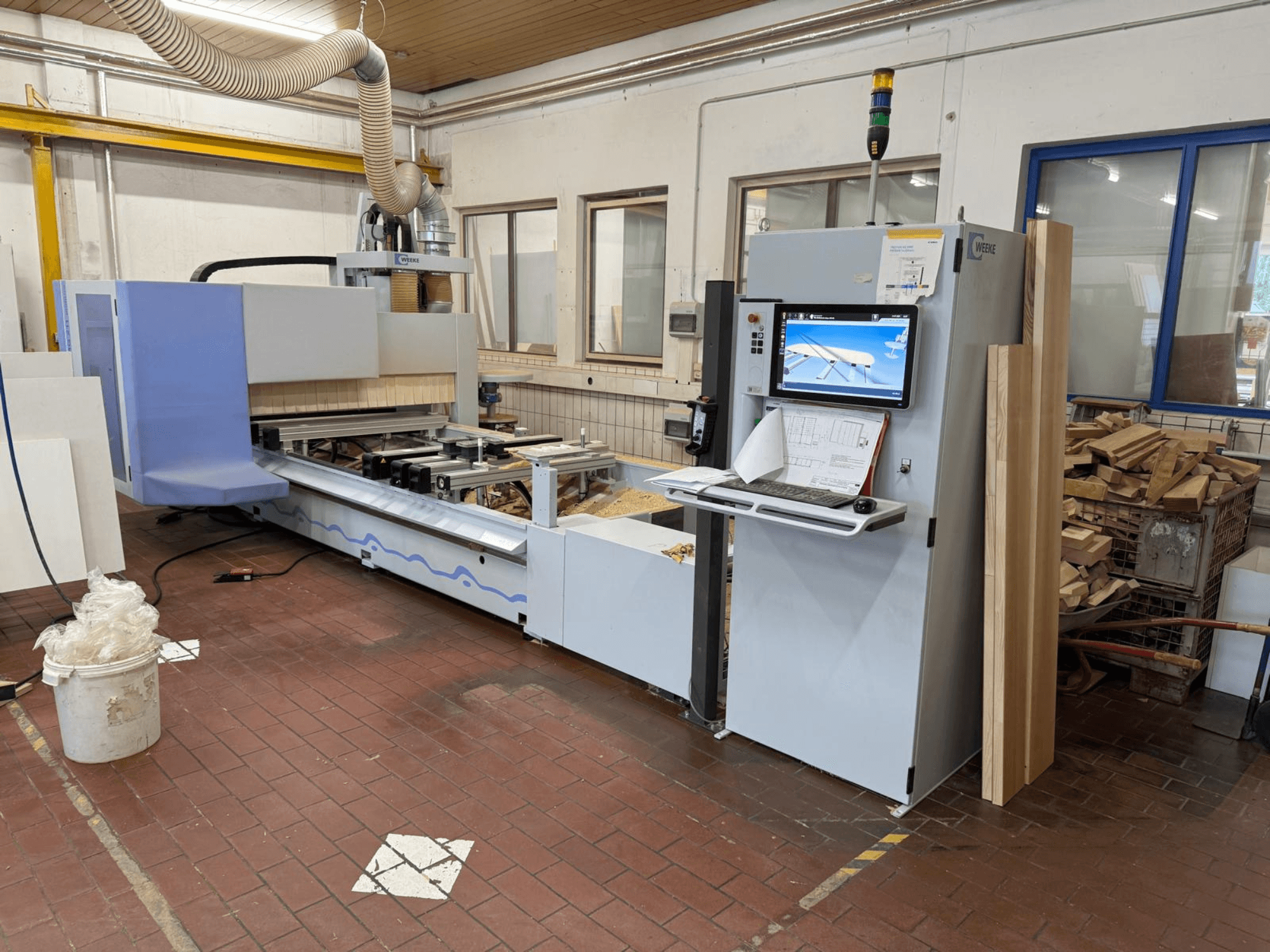 Centro de usinagem de madeira CNC Weeke PROFI BMG211/32/12/K, vista frontal, com painel de controlo e peças de madeira, equipado com sistema de extração de poeira.