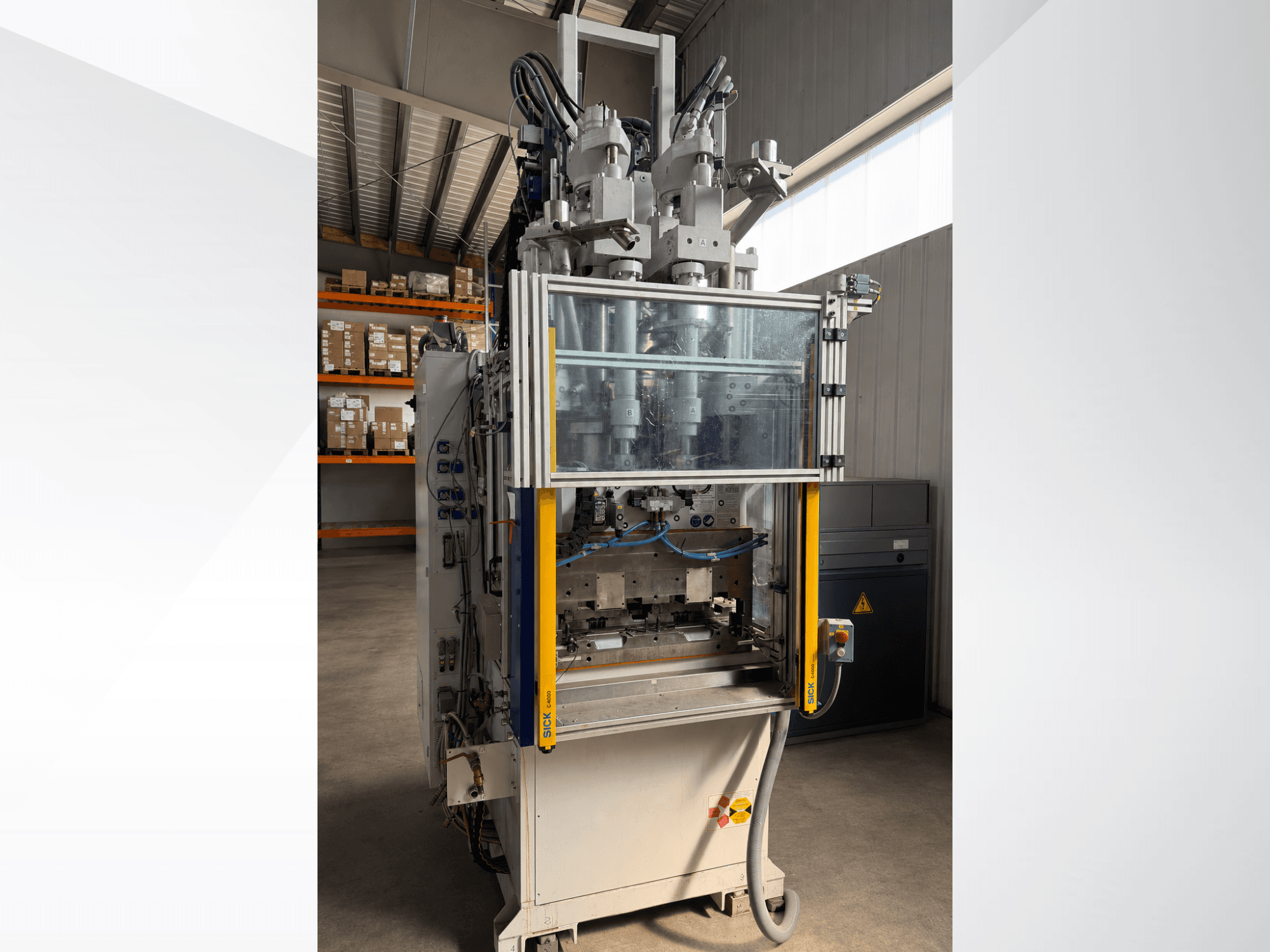 Máquina de moldagem por injeção vertical Battenfeld CM 40, vista frontal com painel transparente, mostrando o painel de controlo e os componentes de injeção.