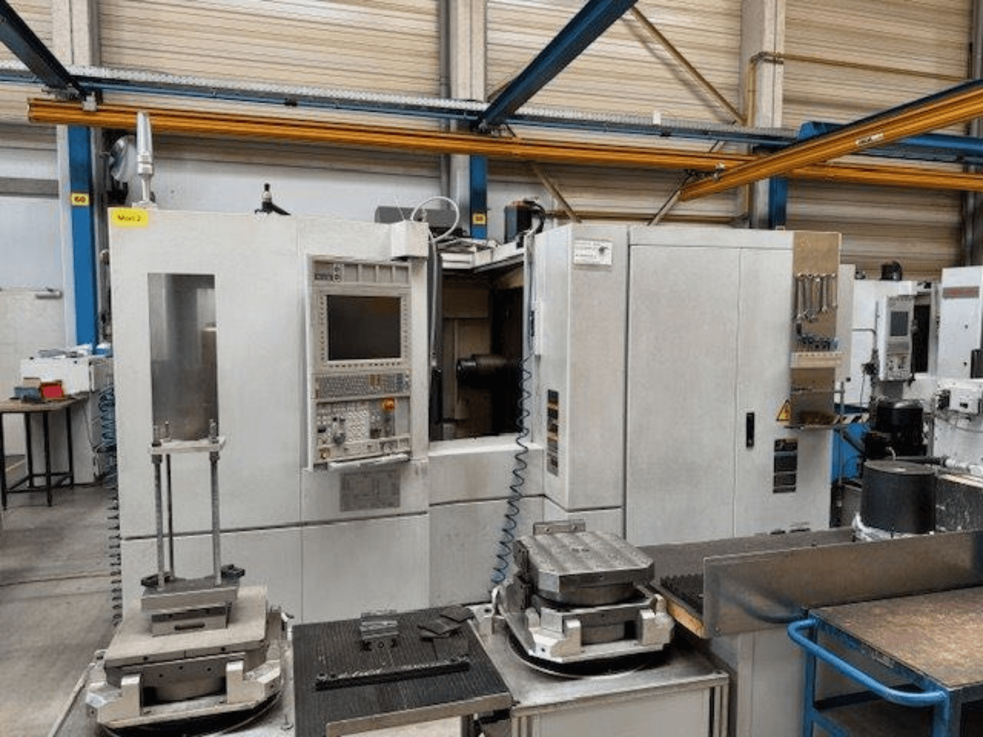MORI SEIKI NH4000 DCG vista frontal de um centro de maquinação horizontal com painel de controlo e peças sobre a mesa.